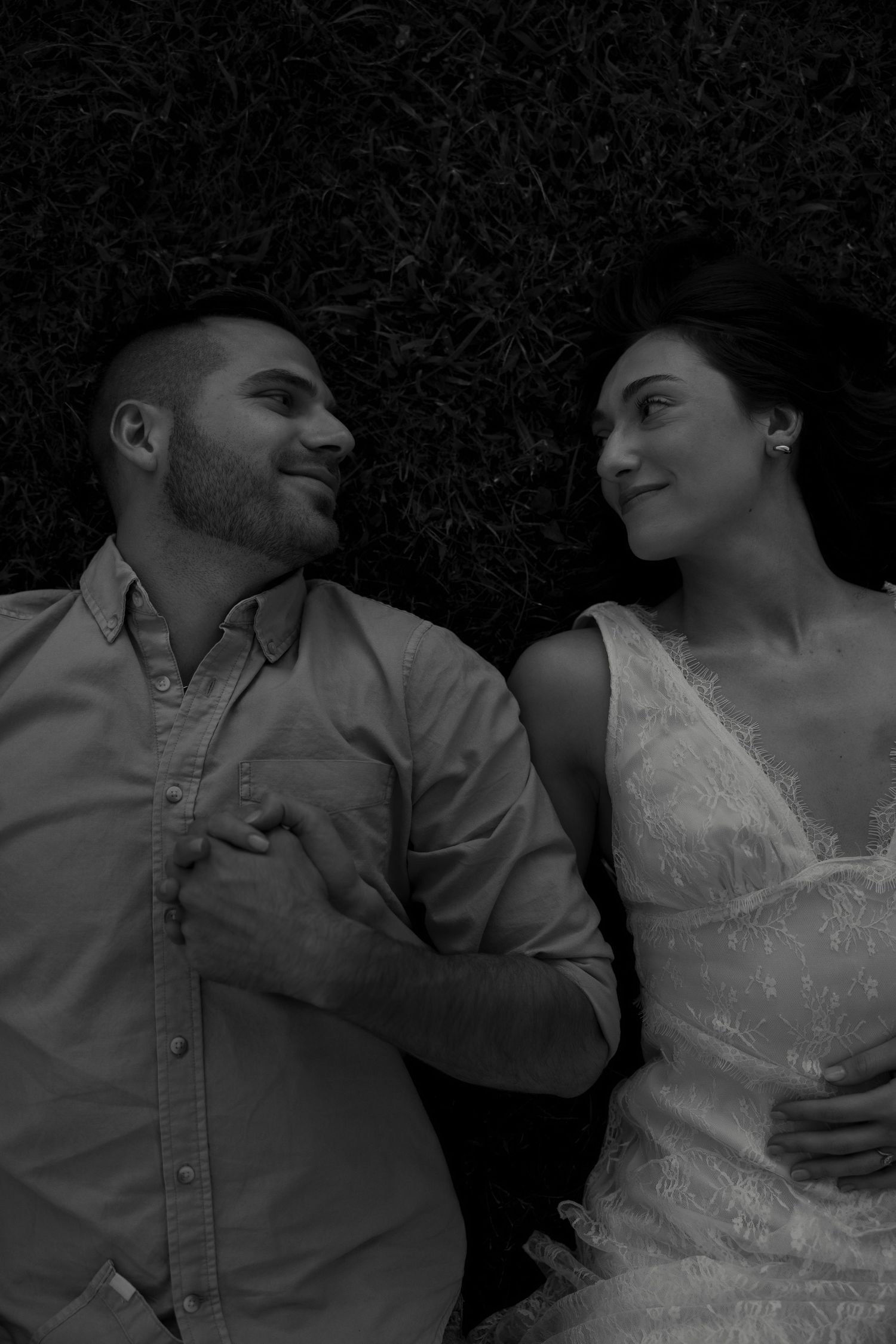 Black and white photo of a smiling couple lying on grass, gazing at each other romantically.