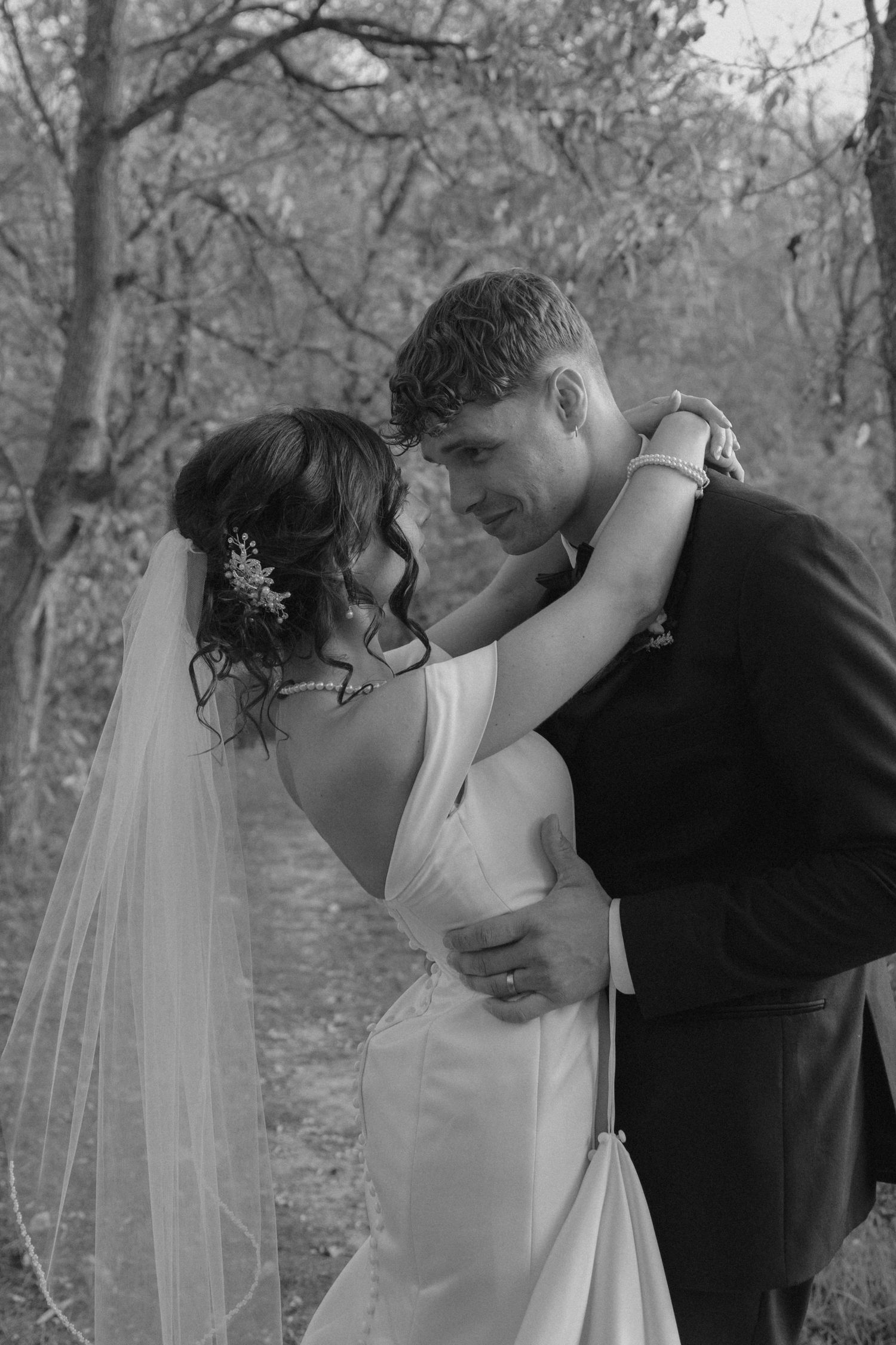 Black and white romantic portrait of bride and groom embracing tenderly among bare autumn trees.