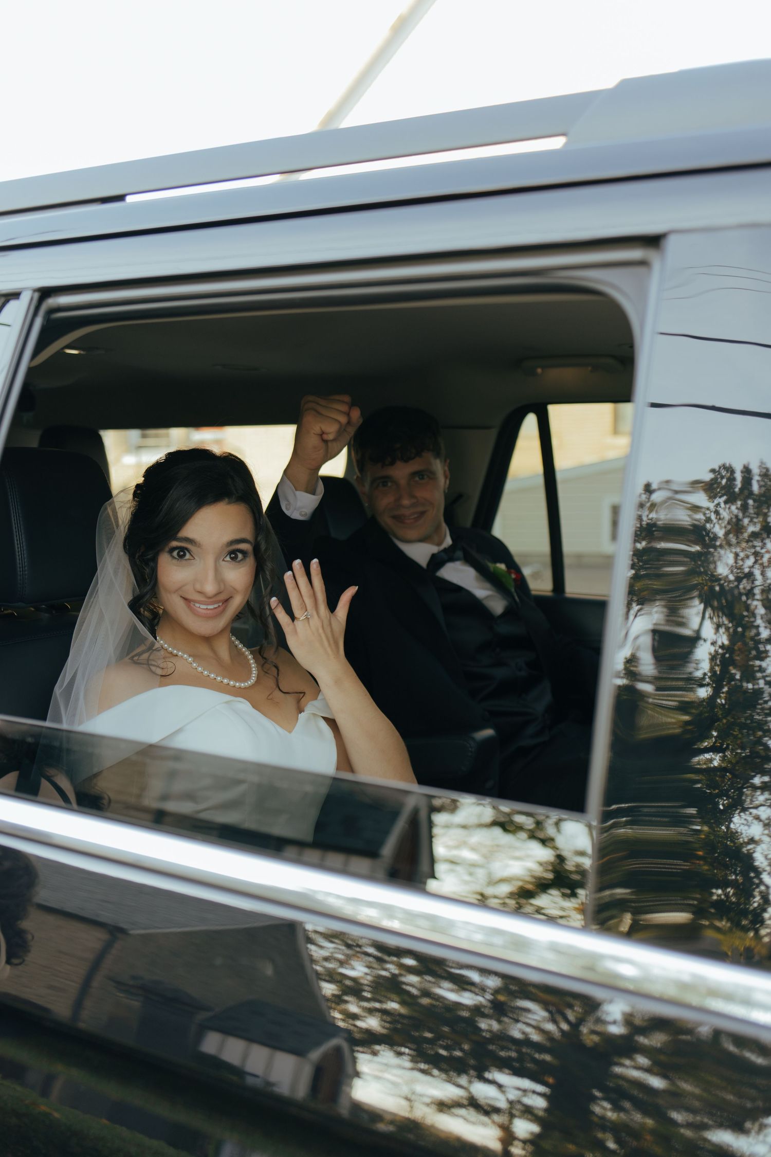 Newlyweds wave and celebrate inside a black SUV after their wedding ceremony.