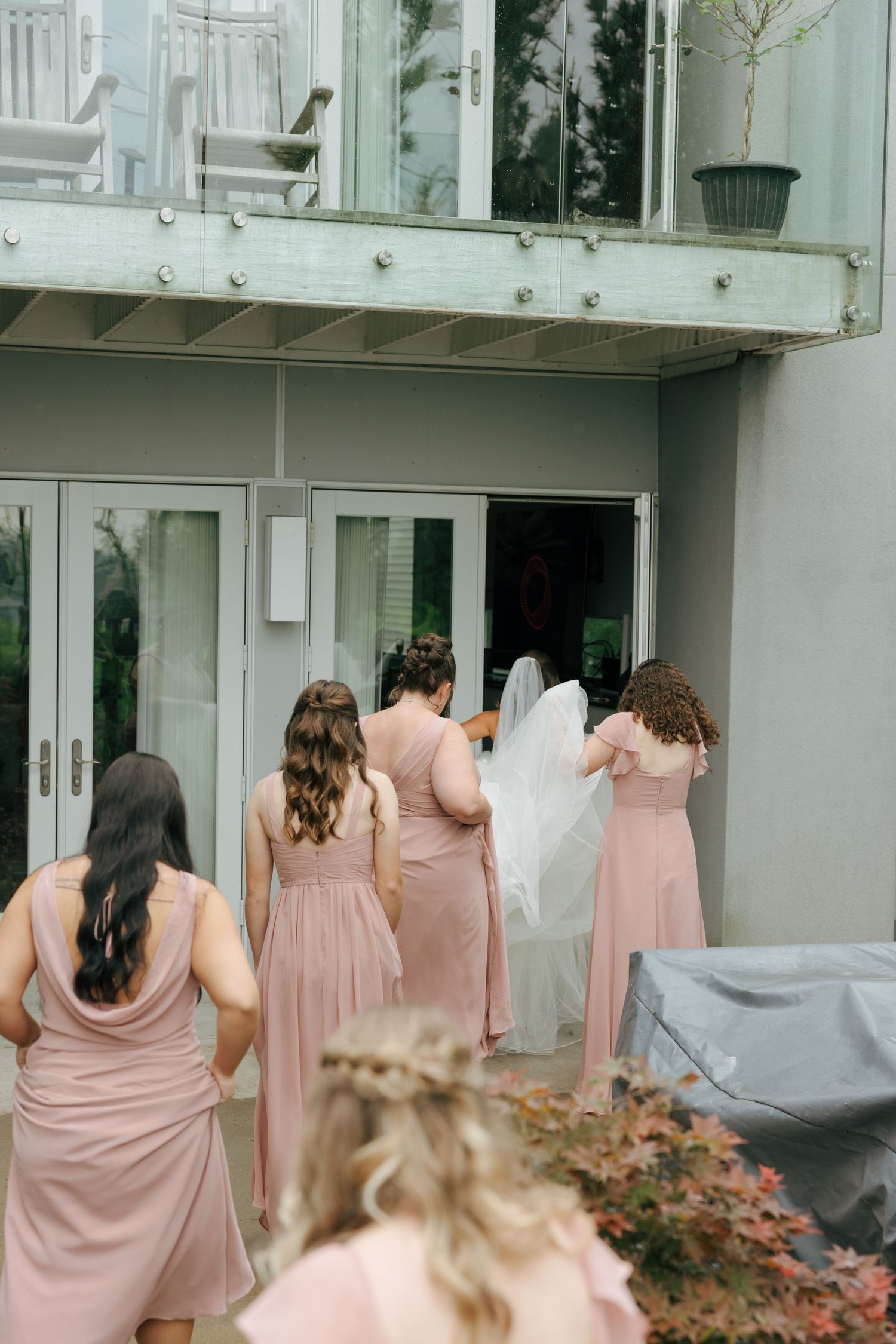 Bridesmaids in pink dresses help bride with veil entering elegant venue.