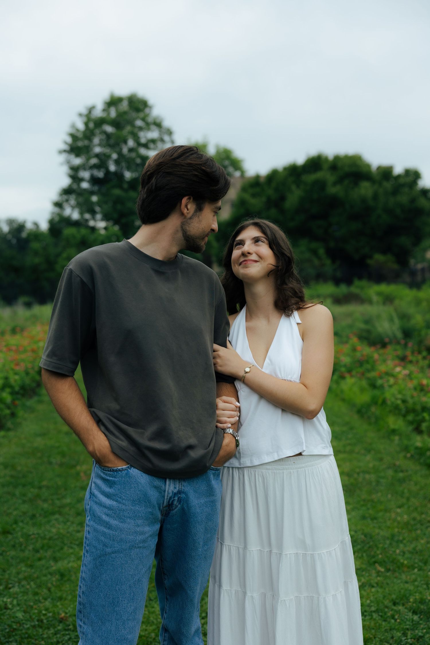 Couple shares a tender moment in a green garden, woman in white dress gazing up at her partner lovingly.