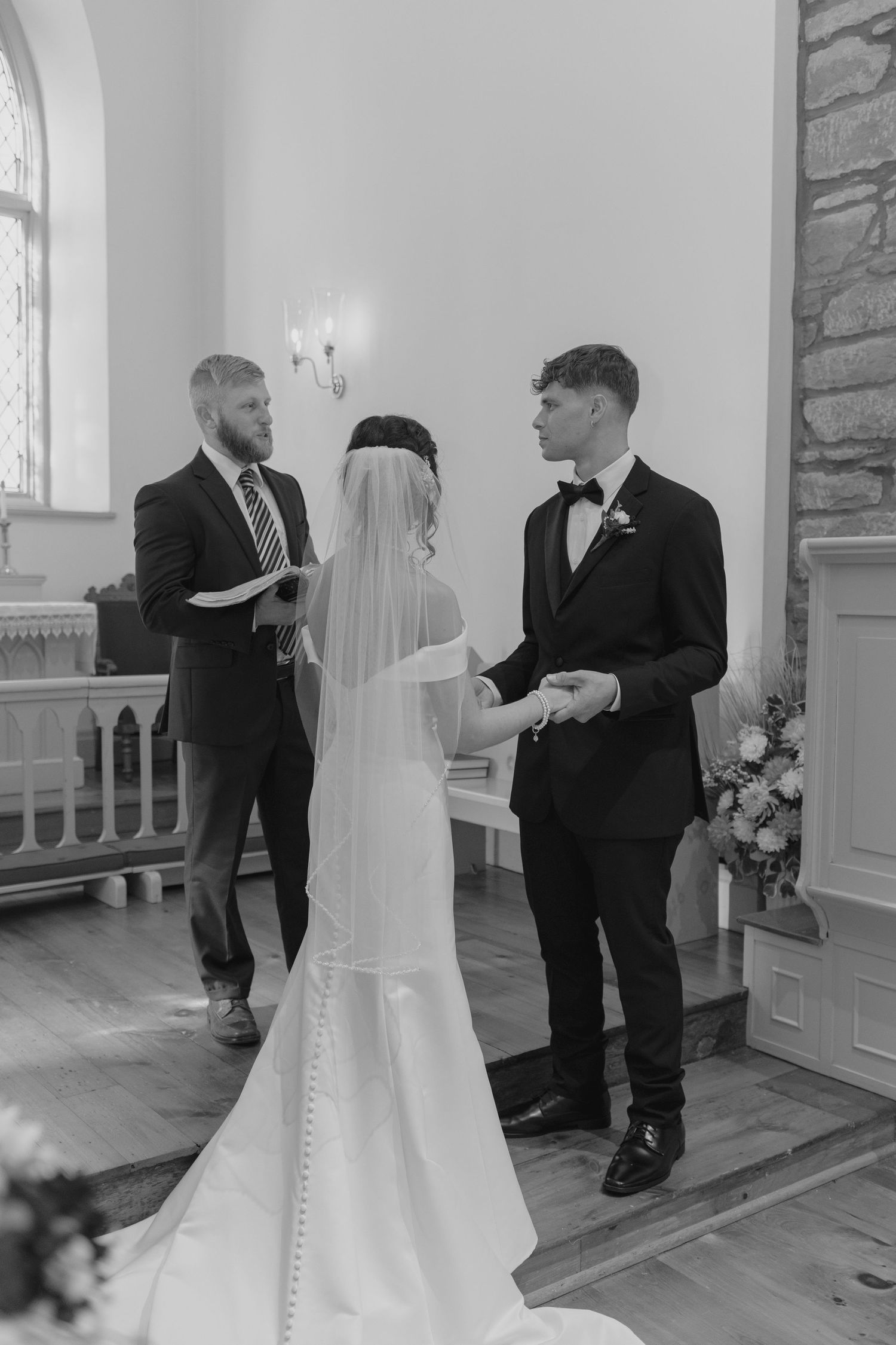 Bride and groom exchange vows at church altar in black and white wedding ceremony photo with officiant.