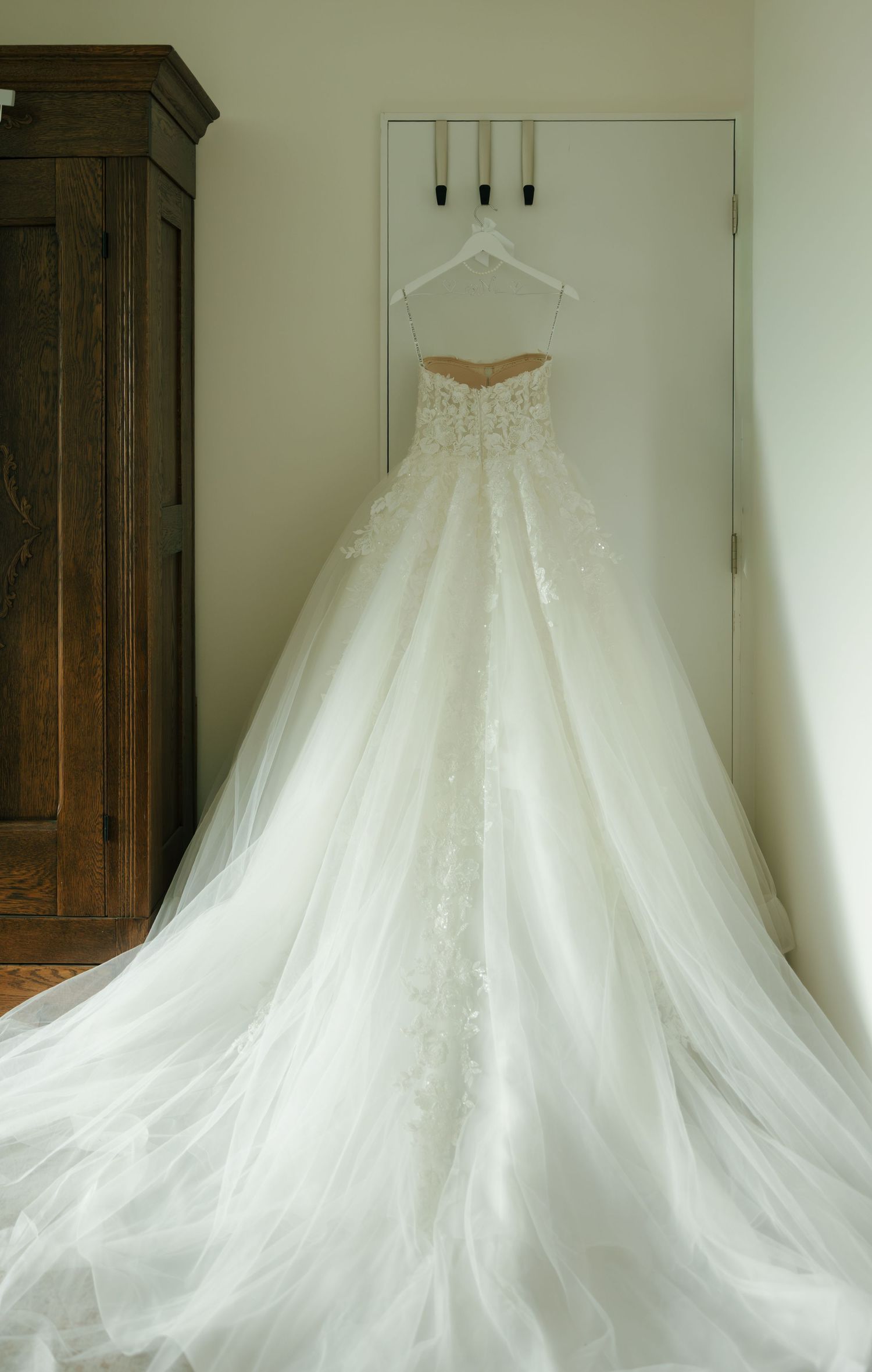 Elegant strapless ball gown wedding dress with lace appliques and long train hanging on a wall hook.