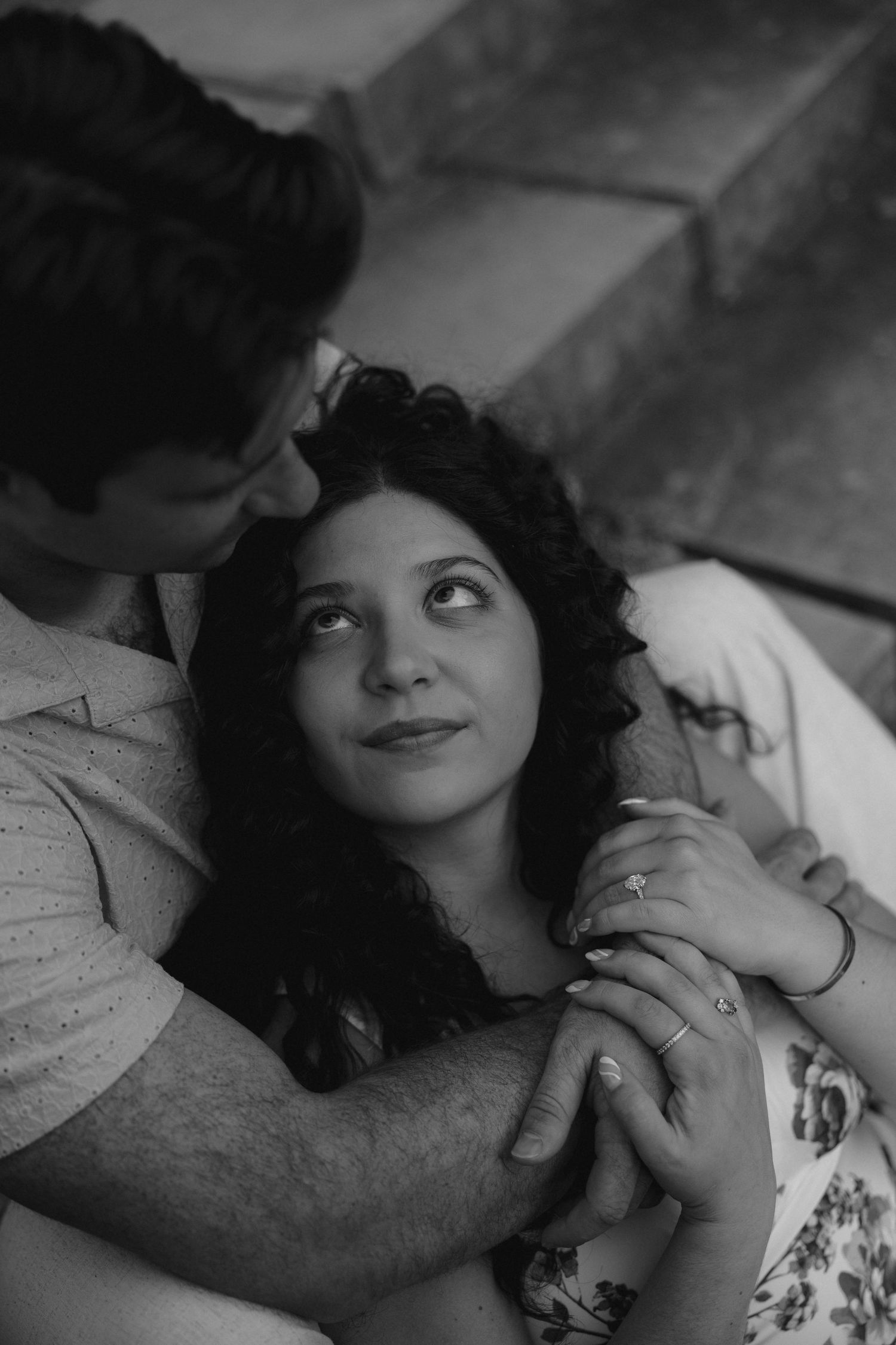 Black and white photo of woman gazing up lovingly at man while he holds her hands on steps.