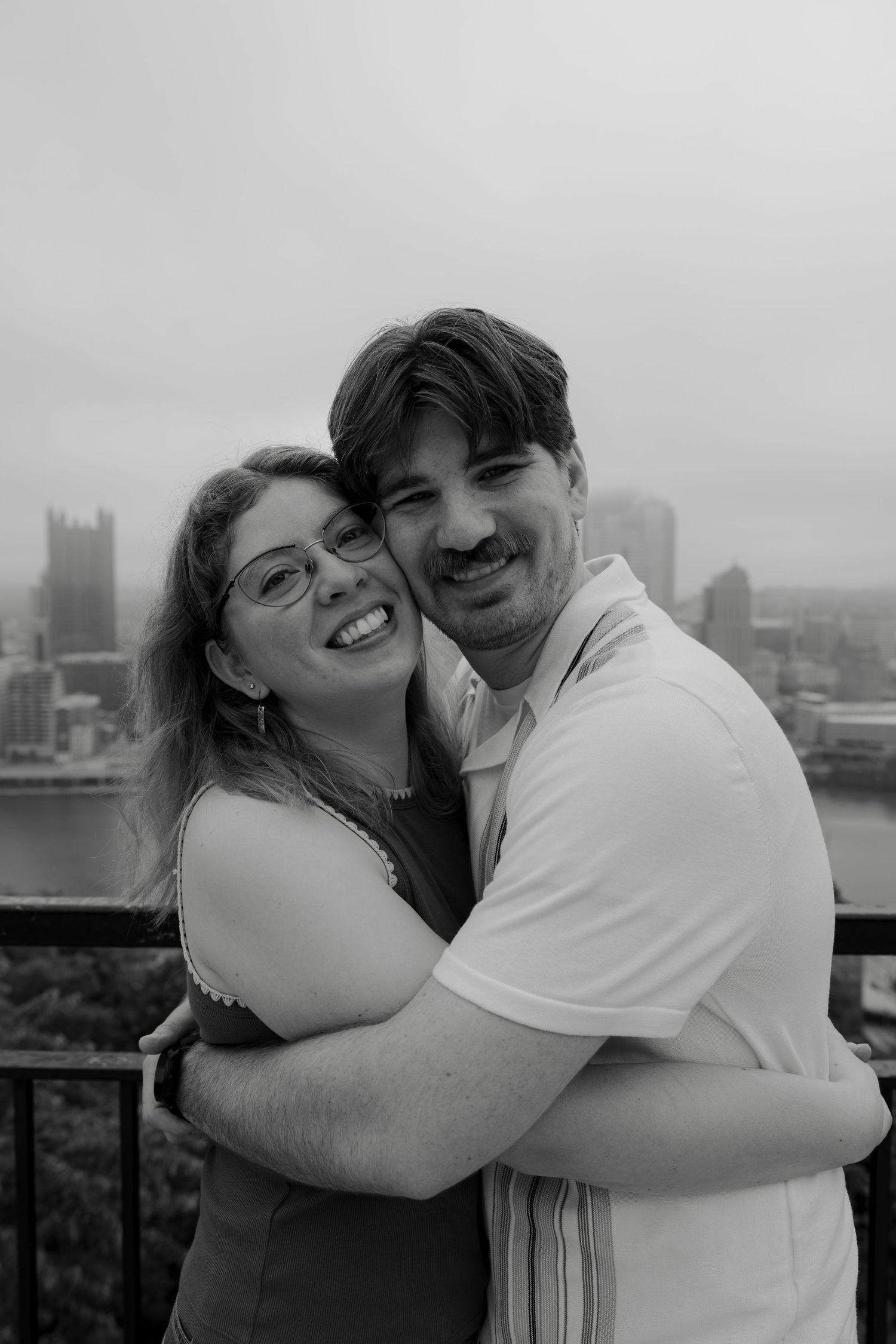 Happy couple hugging and smiling on a rooftop with city skyline behind them in black and white photo.