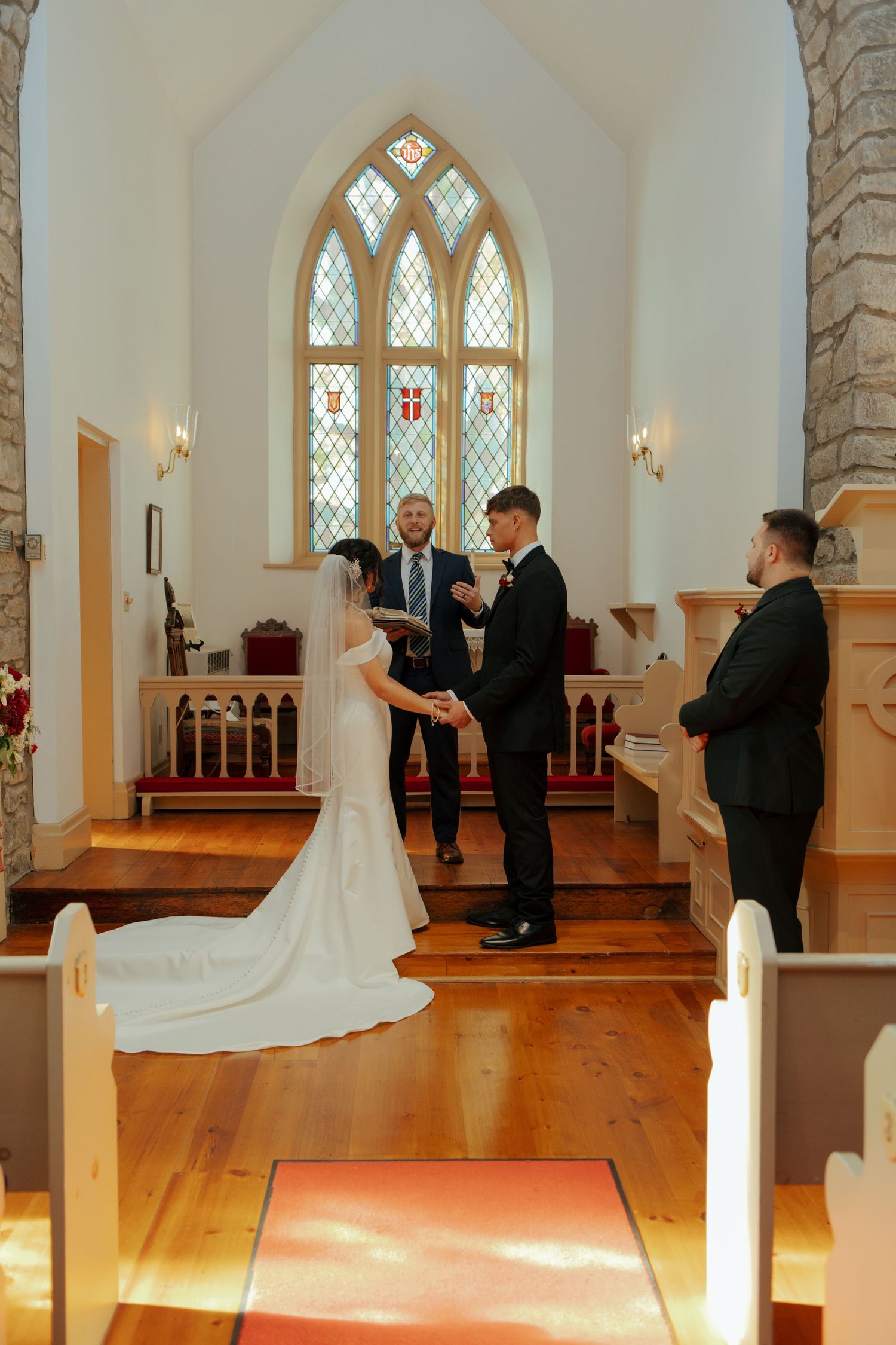 Bride and groom exchanging vows at altar of stone chapel with stained glass windows.