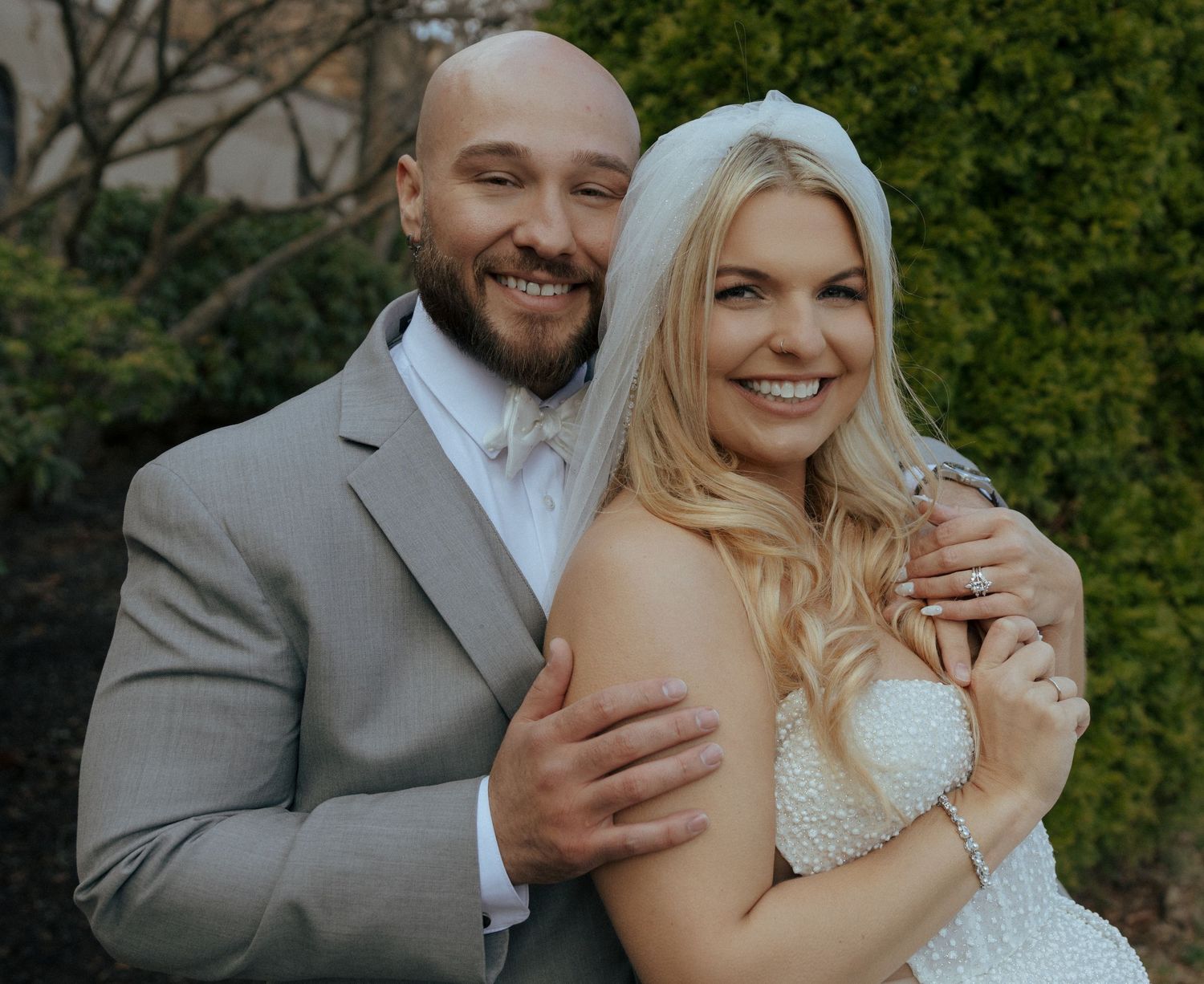 A happy couple embraces and laughs together during their outdoor wedding photo session with greenery in background.