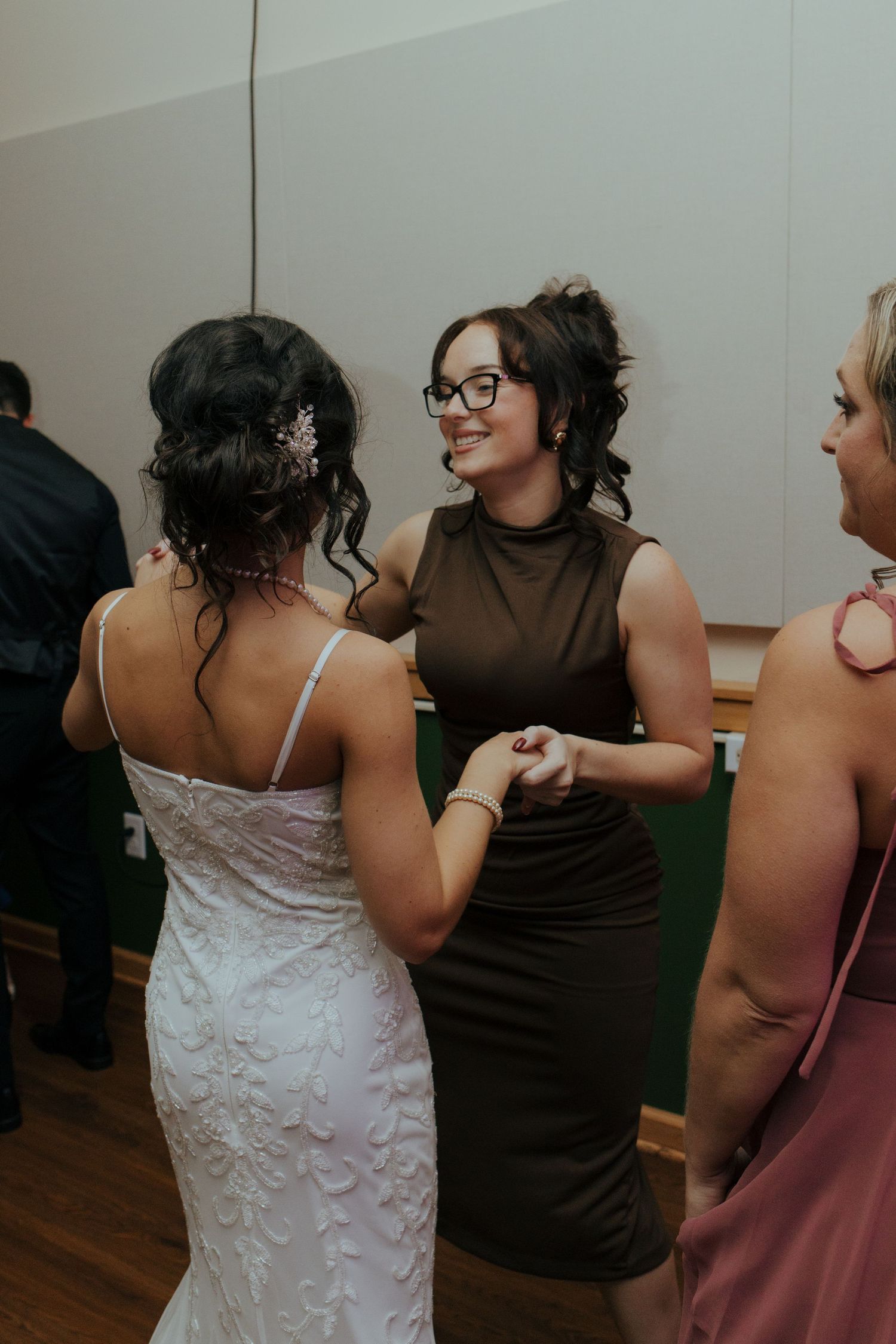 Bride in lace gown holding hands with a smiling guest in an olive dress at the wedding reception.