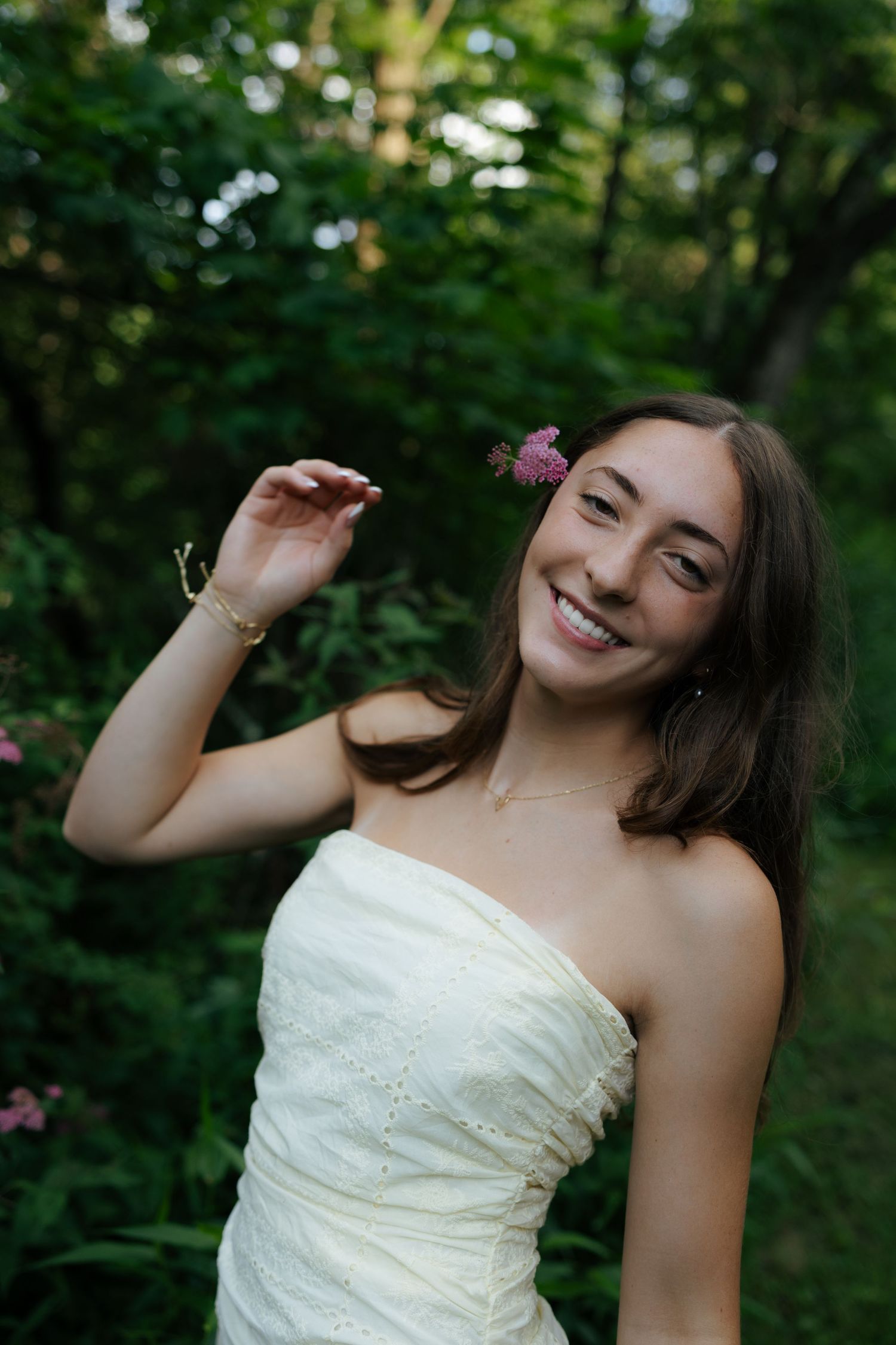 Happy young woman in strapless dress holding pink wildflower outdoors.