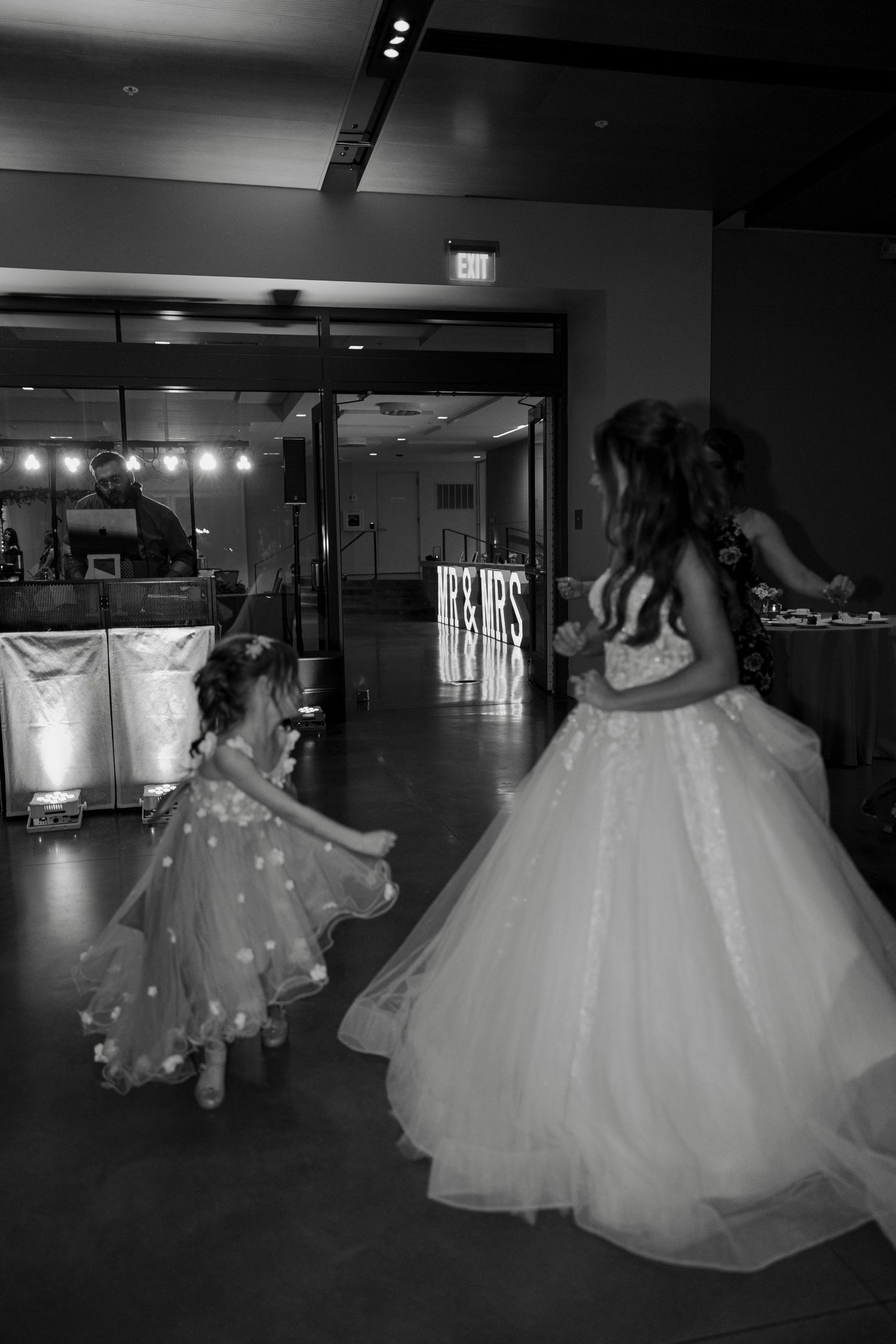 Black and white photo of flower girls in tulle dresses dancing at an elegant wedding reception venue.