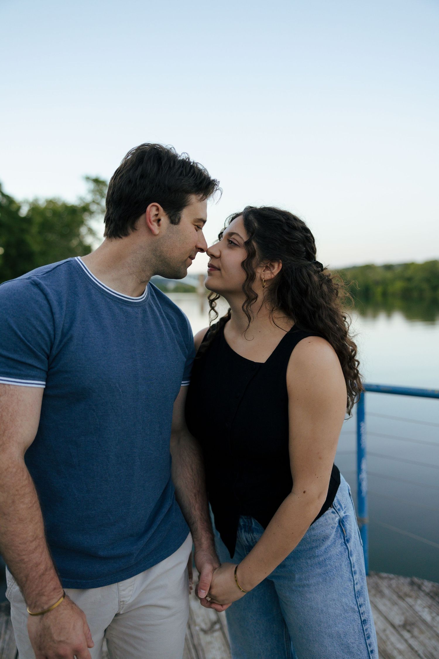 Romantic couple holding hands and sharing a tender moment near a serene river at dusk.
