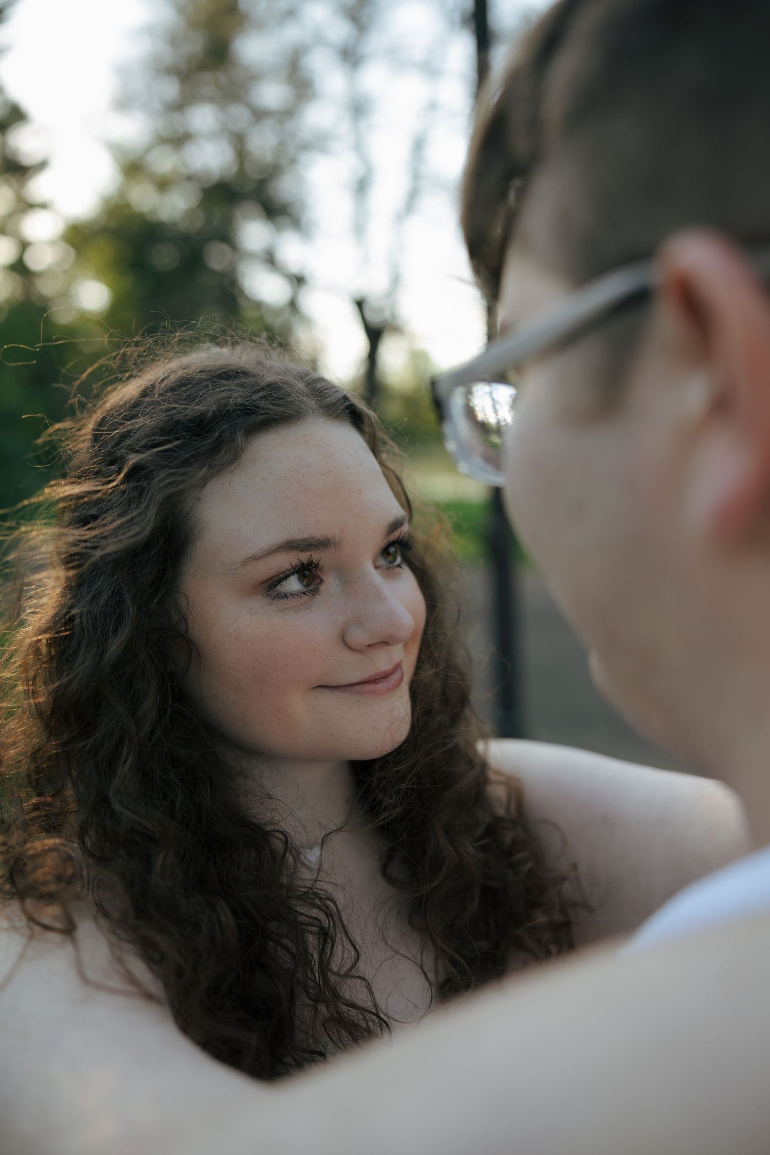 Young woman with curly hair smiling softly at her partner outdoors in golden light.