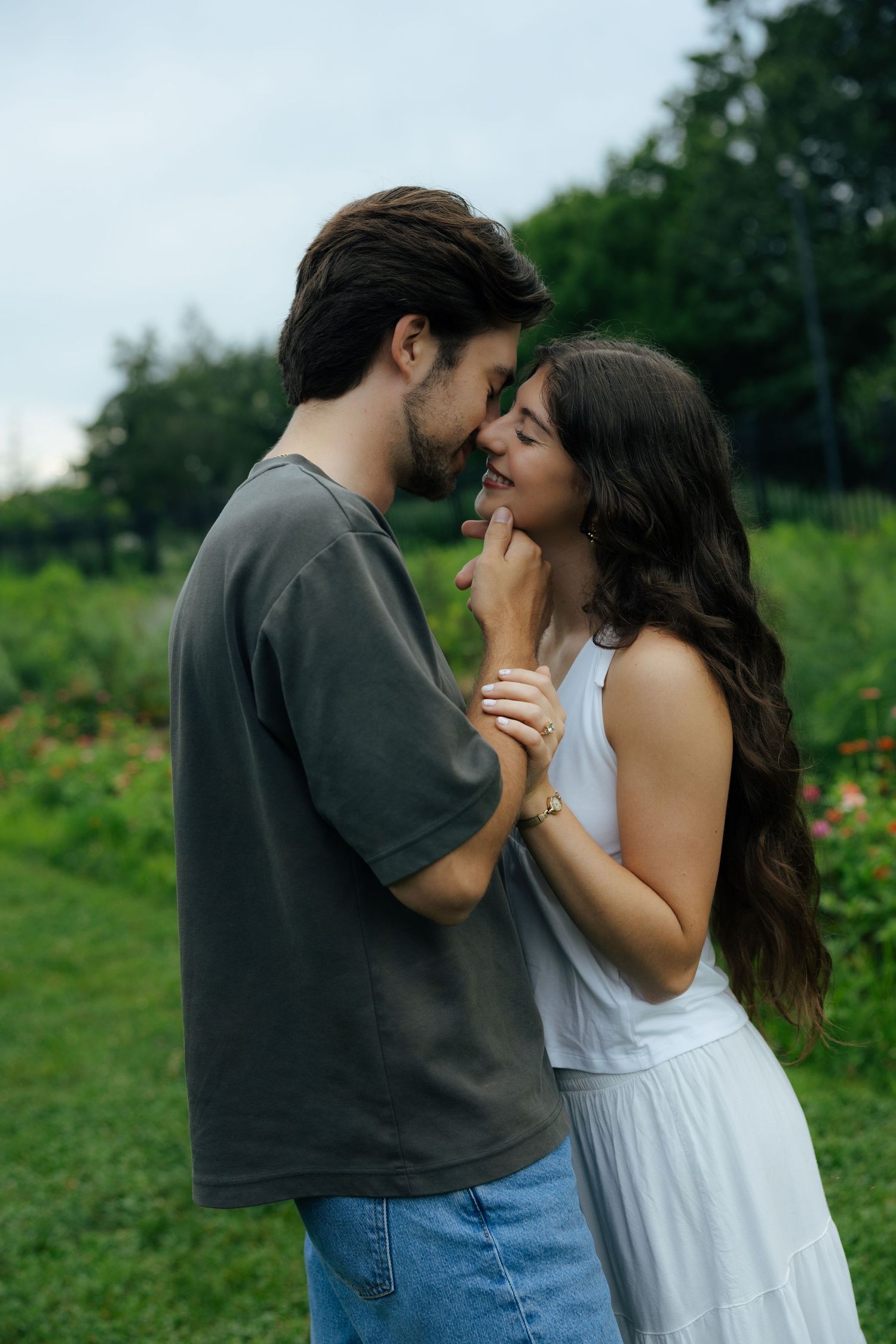 Happy engaged couple nearly kissing while standing in a green garden, woman in white dress.