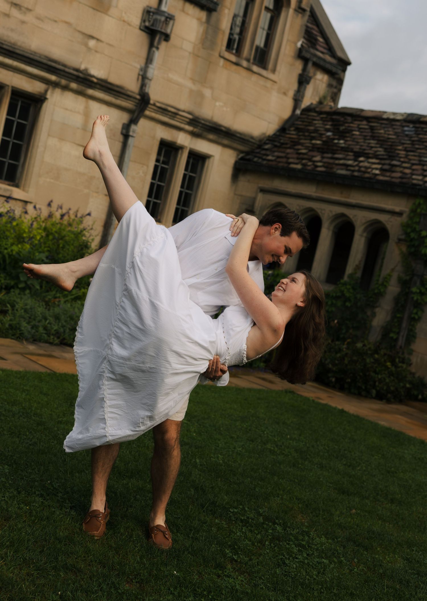 Romantic couple sharing a dip kiss on green lawn outside an elegant stone estate building.