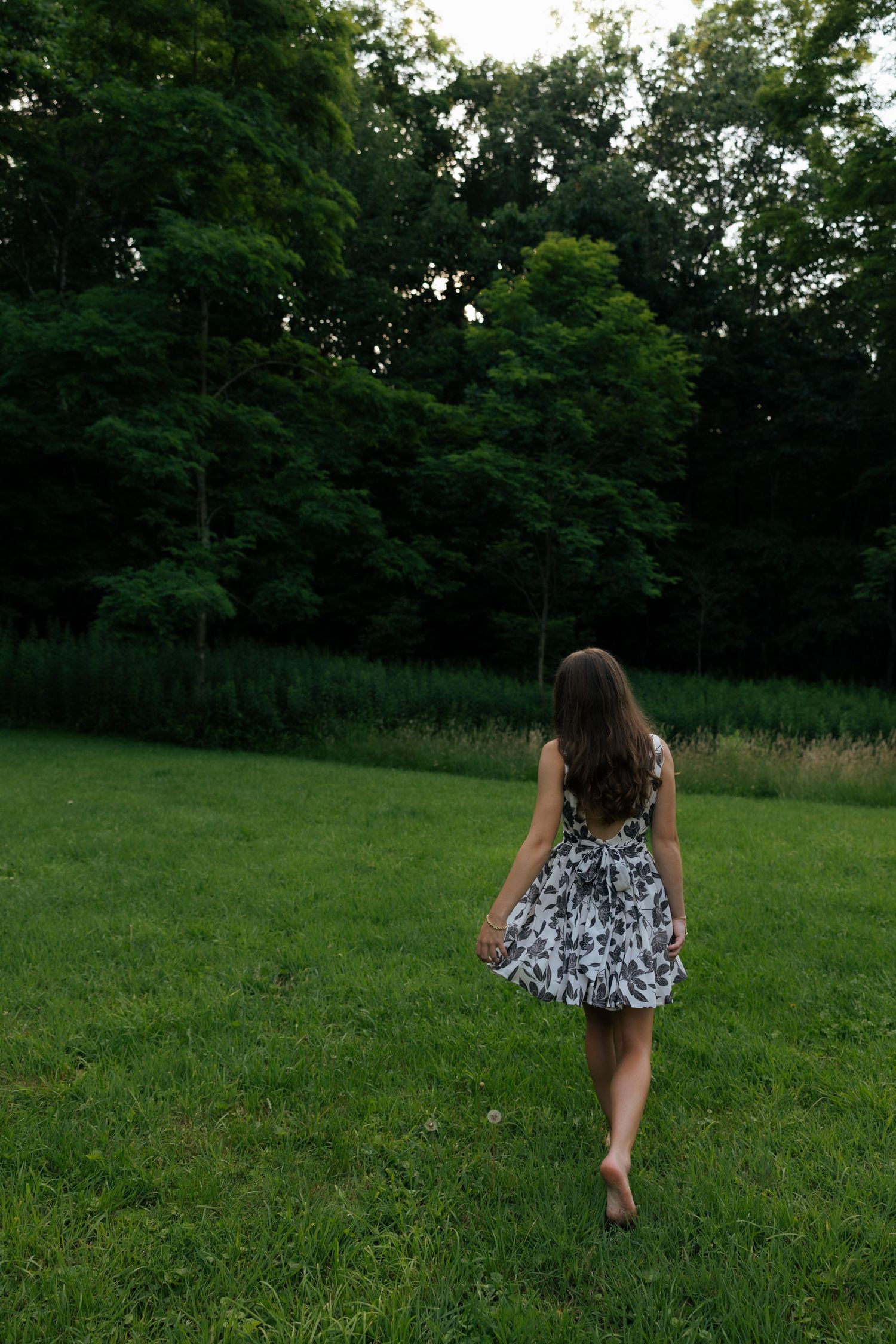 Woman in floral dress walking barefoot across lush green lawn.
