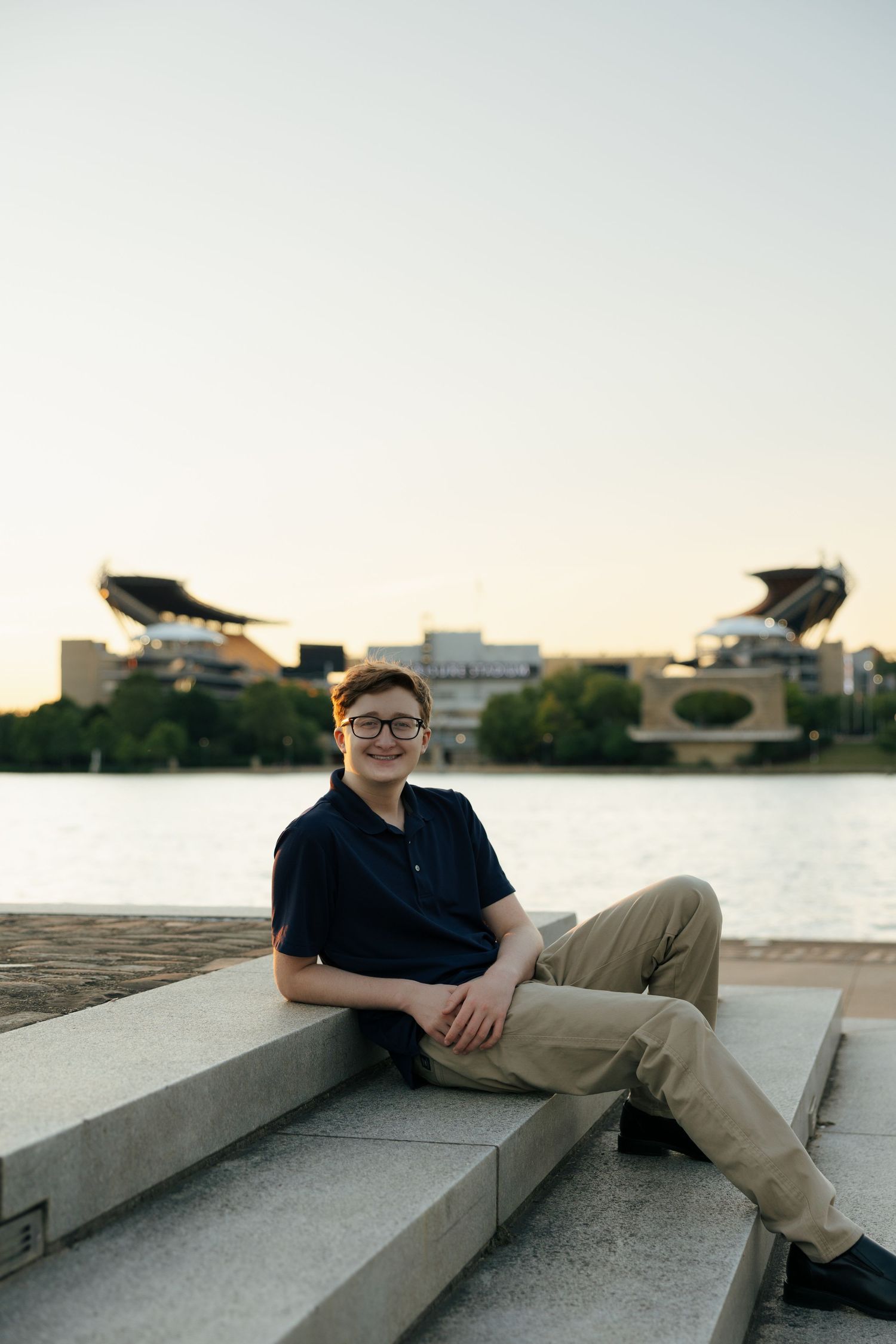 Teen boy relaxing on stone steps with stadium across river.