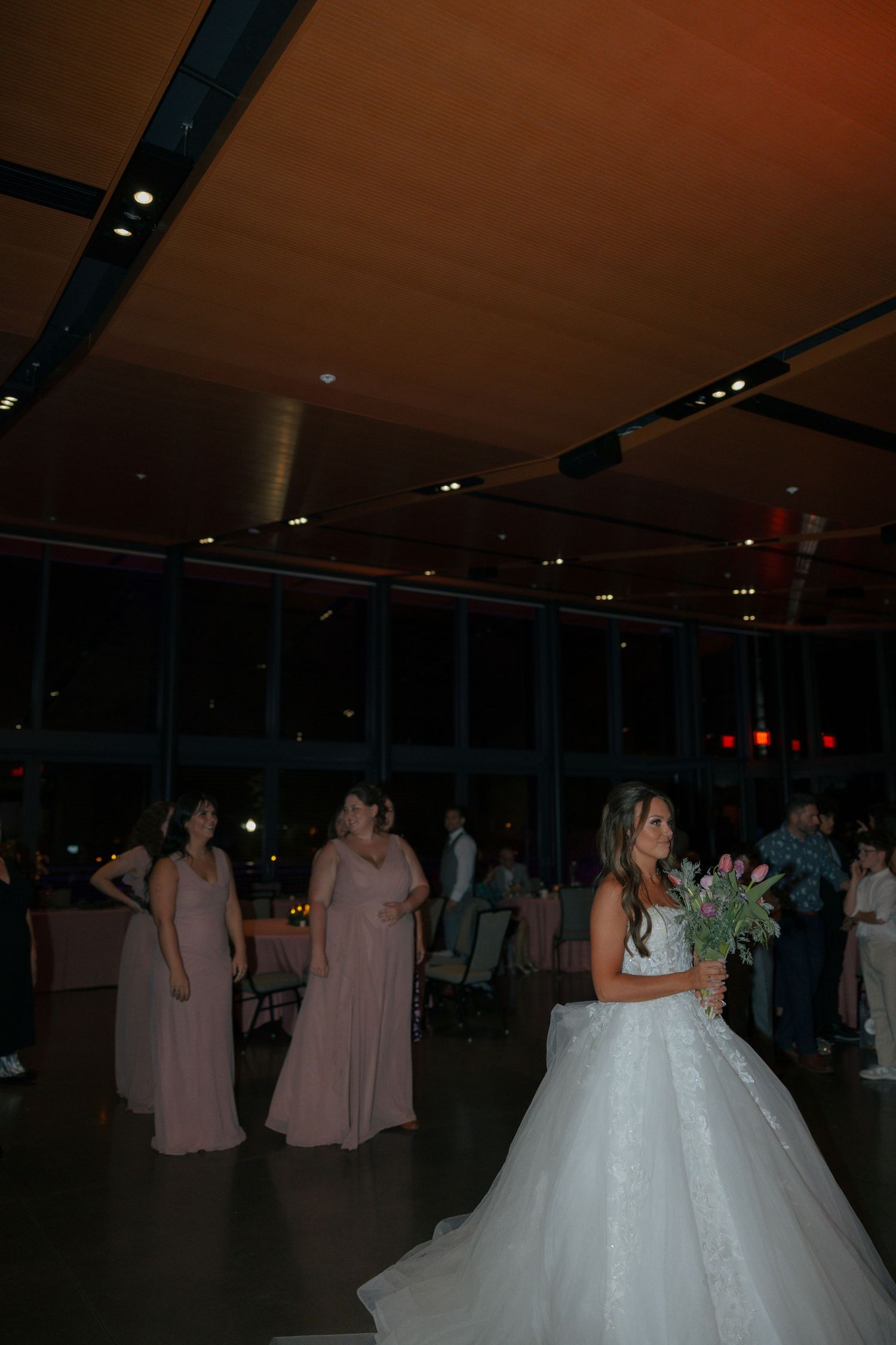 Bride in white gown prepares to toss bouquet to bridesmaids in pink dresses at wedding reception.