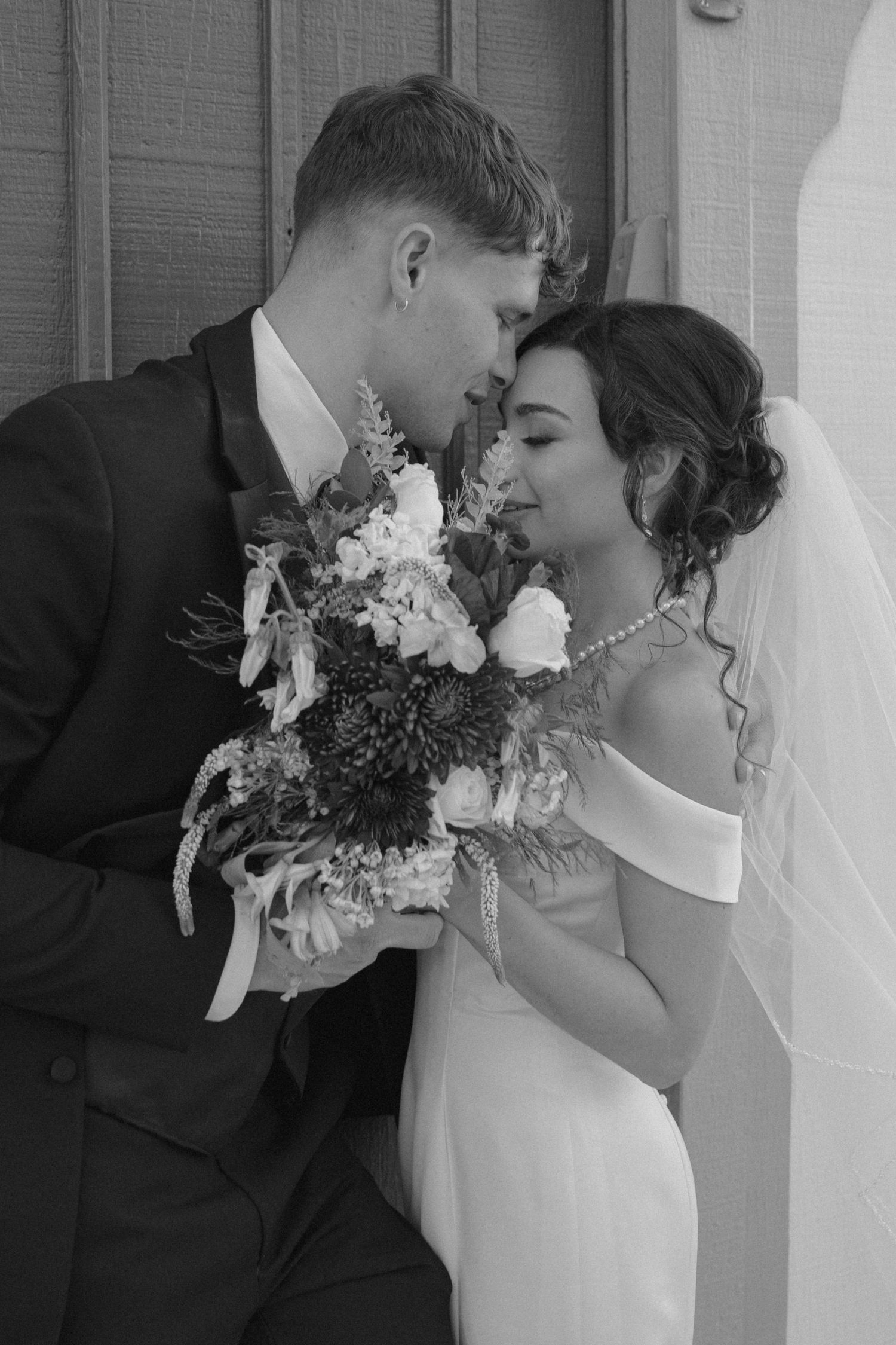 Black and white romantic portrait of bride and groom sharing intimate moment with wedding bouquet.