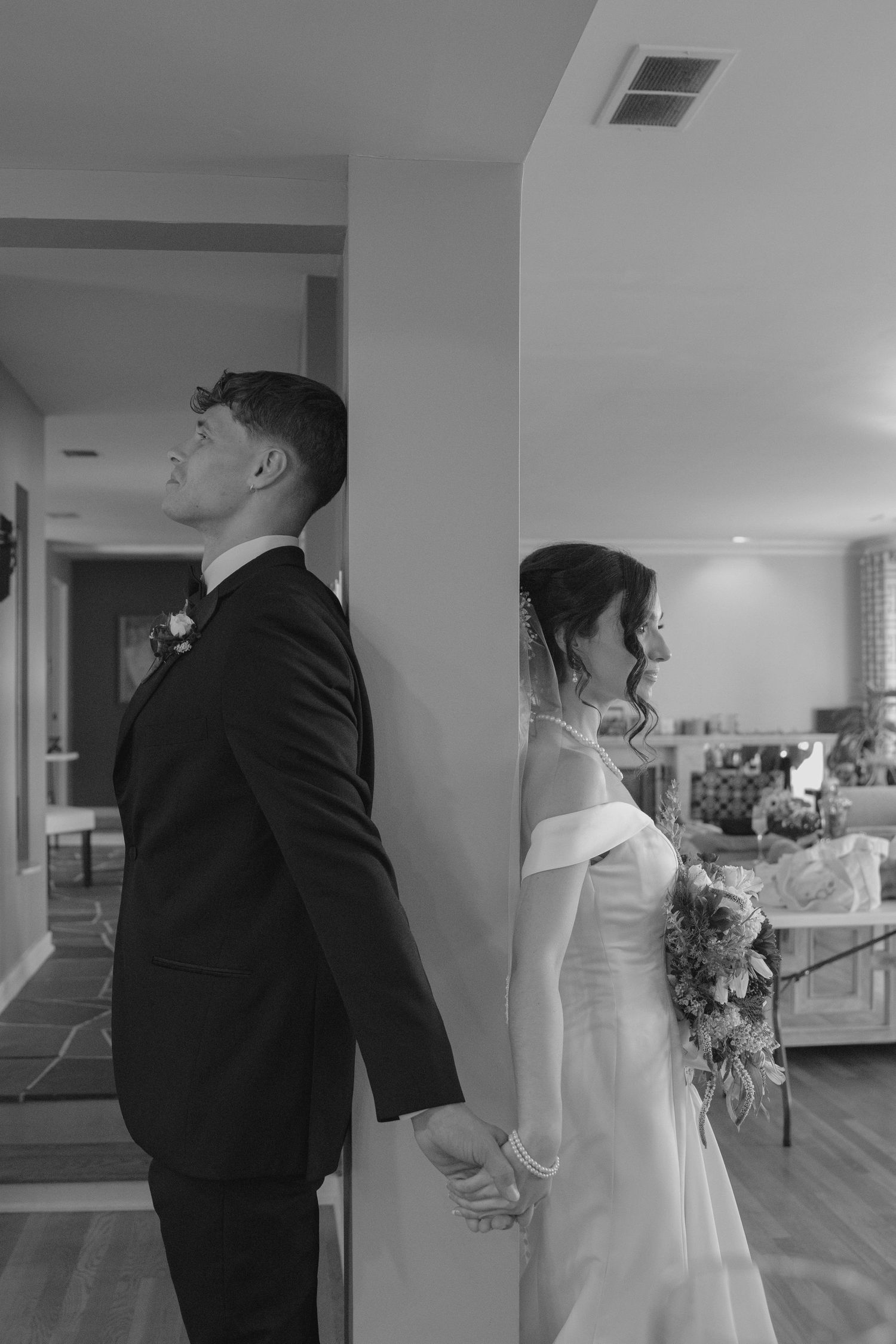 Bride and groom holding hands around corner in black and white first look wedding photo.