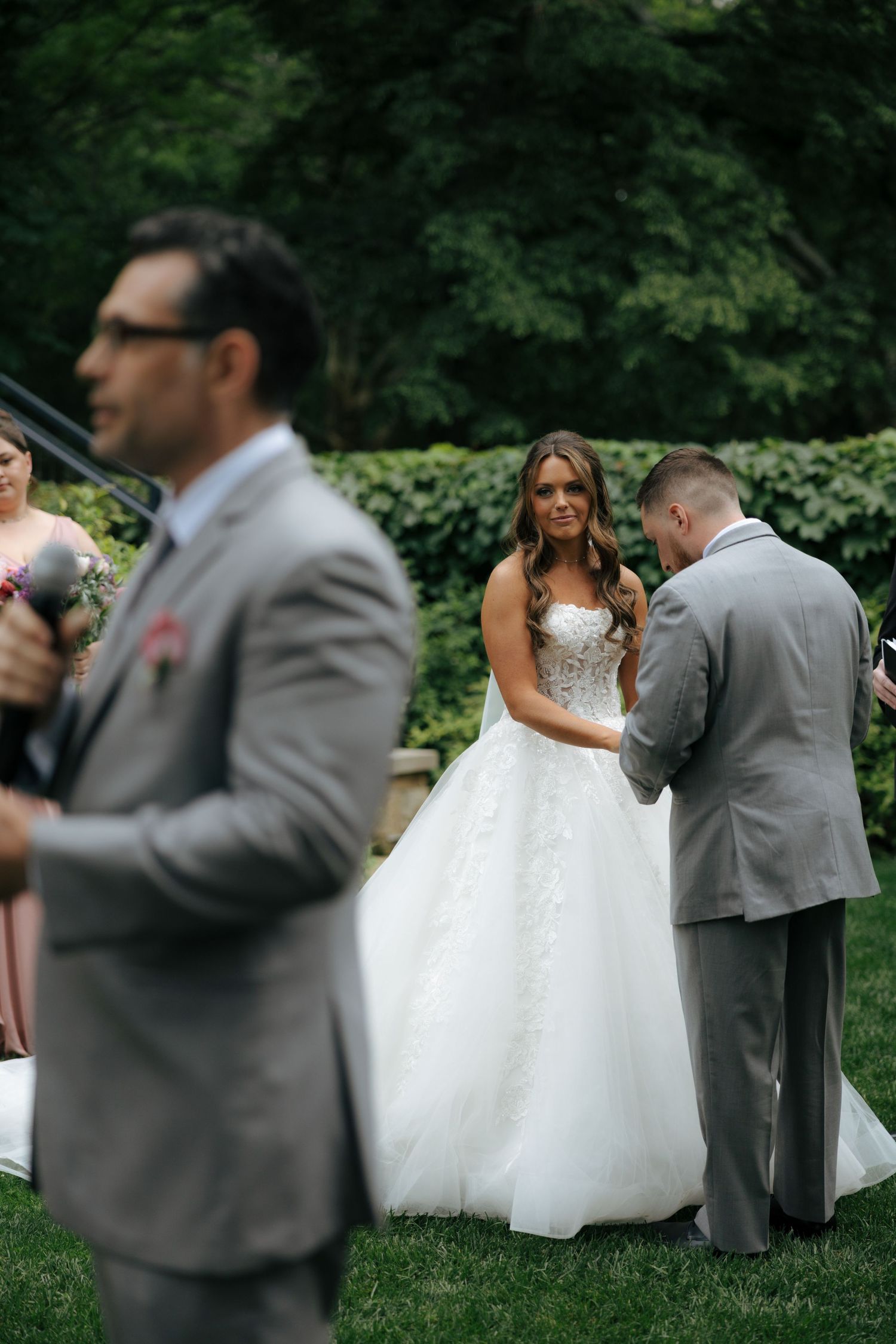 Bride in a white ballgown holds hands with groom in gray suit at outdoor wedding.