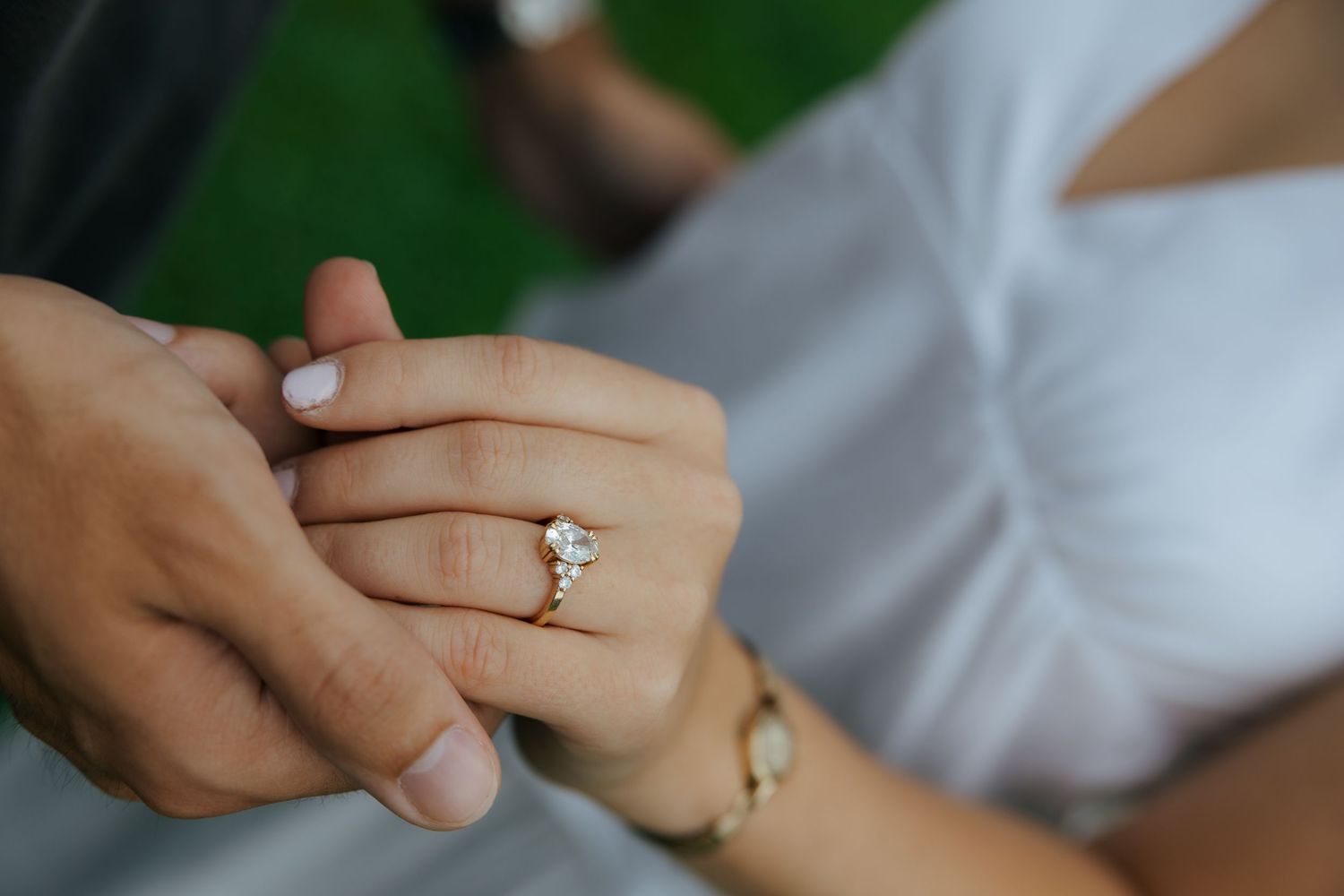 Close-up of a woman wearing a gold diamond engagement ring while holding hands with a man outdoors.