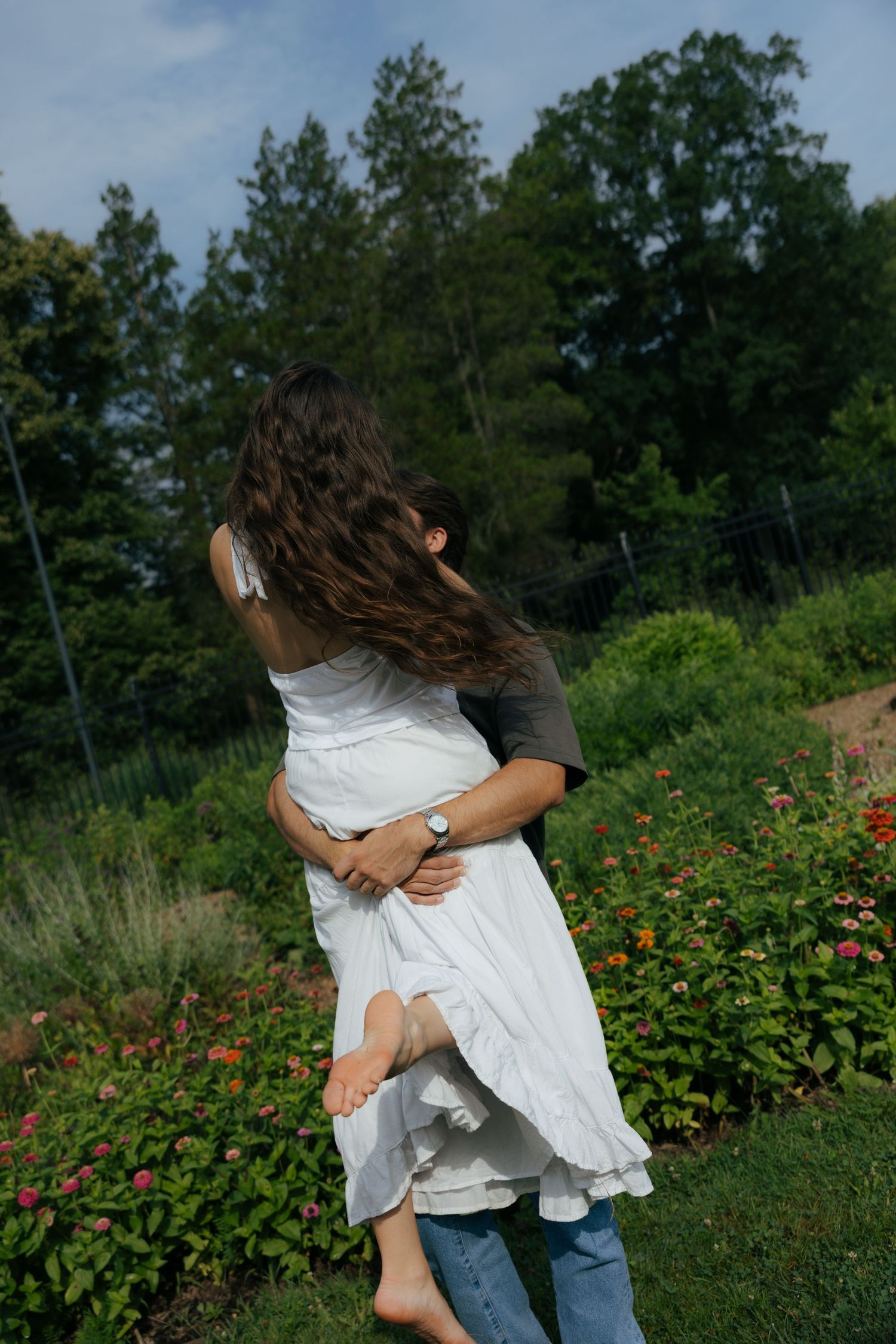 A couple embraces and spins in a lush garden, the woman's long hair flowing as she is lifted off the ground.