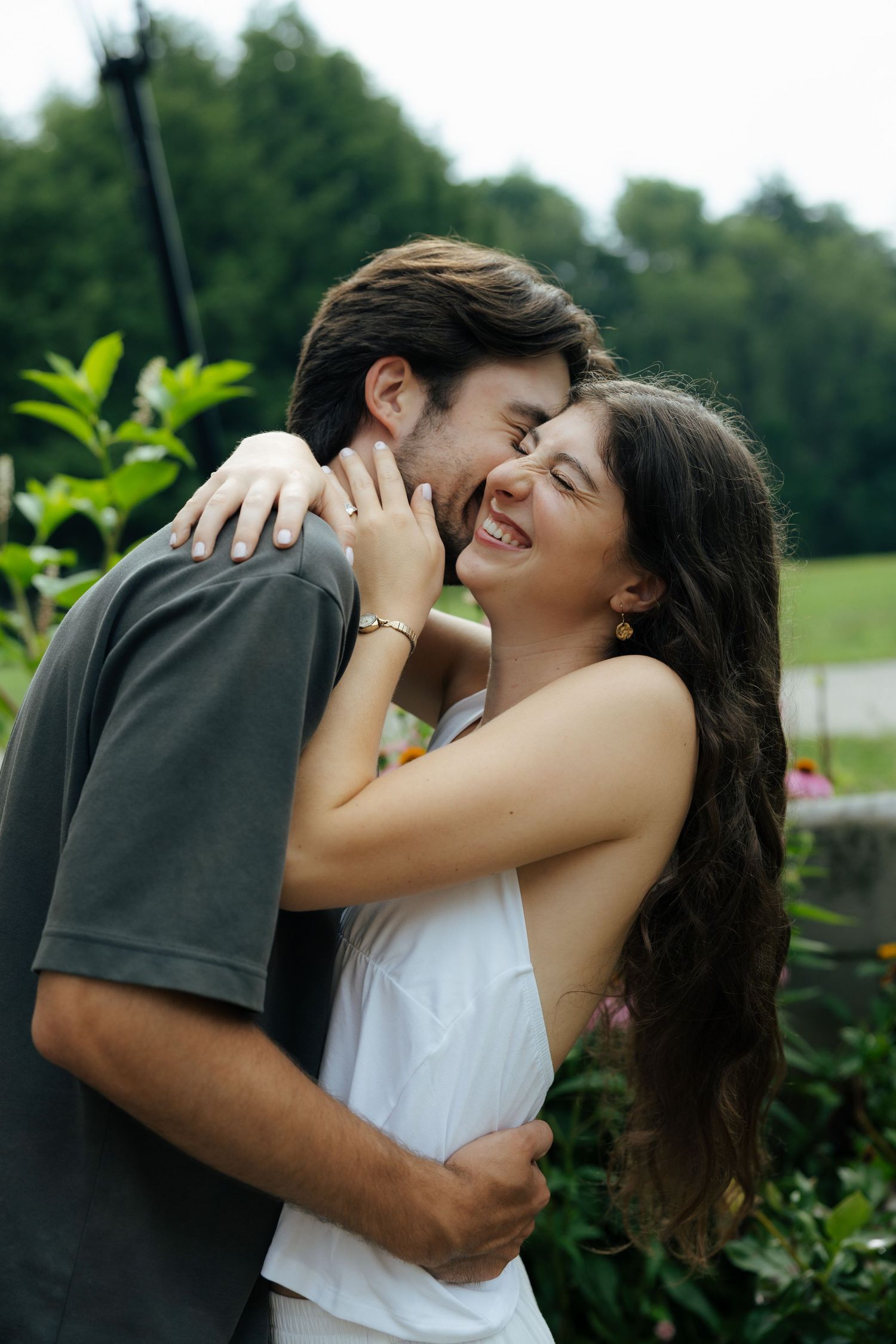 Joyful couple embracing and laughing together surrounded by green foliage in an outdoor garden.