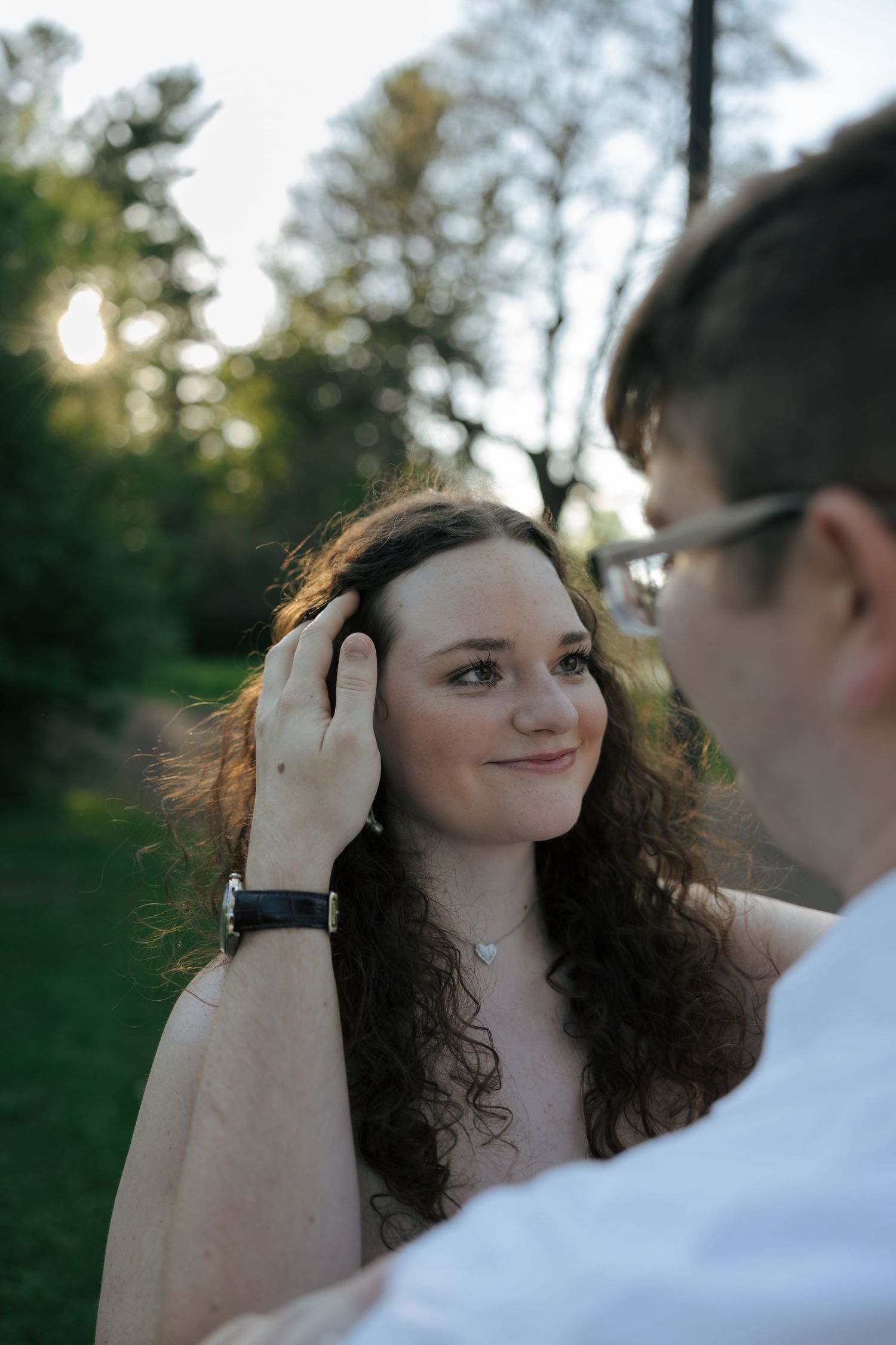 Man gently brushing curly-haired woman's hair back as she smiles softly in golden hour light.