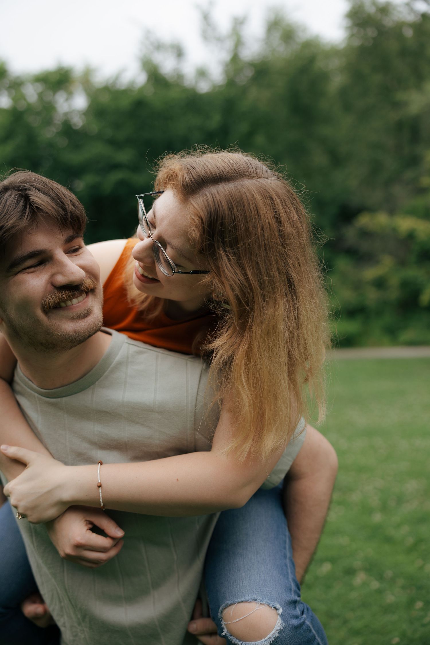 Happy couple sharing a piggyback ride in a lush green park, laughing together outdoors.