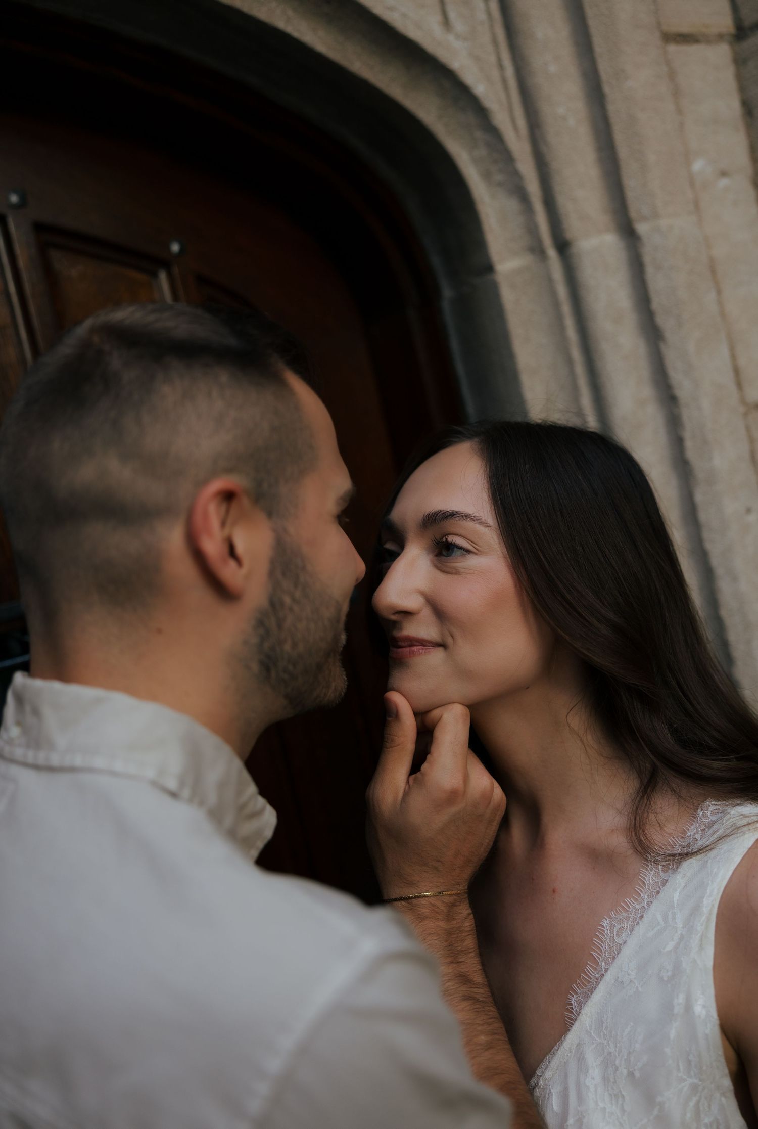 Romantic couple shares tender moment as man gently touches woman's chin near stone archway.