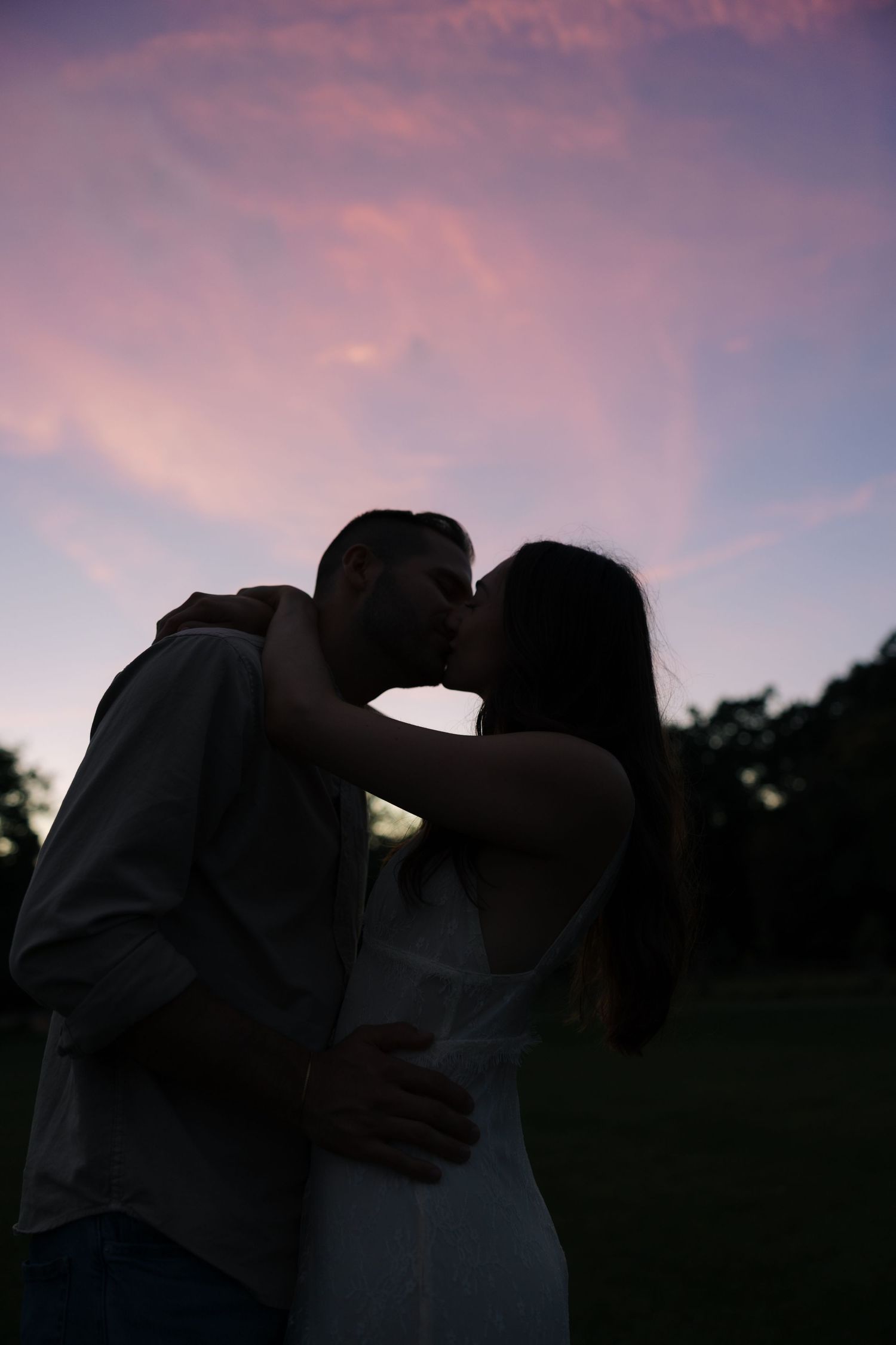 Romantic silhouette of a couple sharing a kiss against a vibrant pink and purple evening sky.