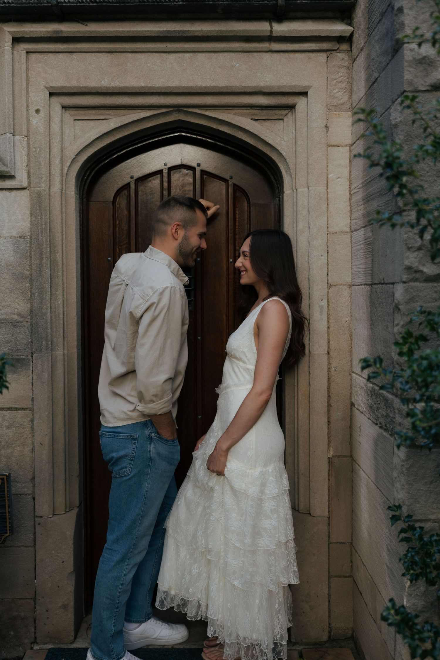 Couple shares romantic moment in front of arched wooden door of stone building.