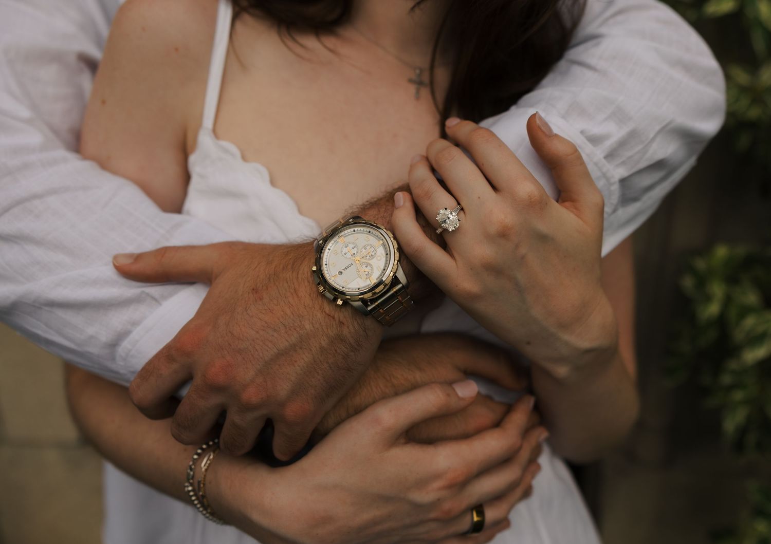 Close-up of couple embracing, showcasing a diamond engagement ring and gold watch on her hand.