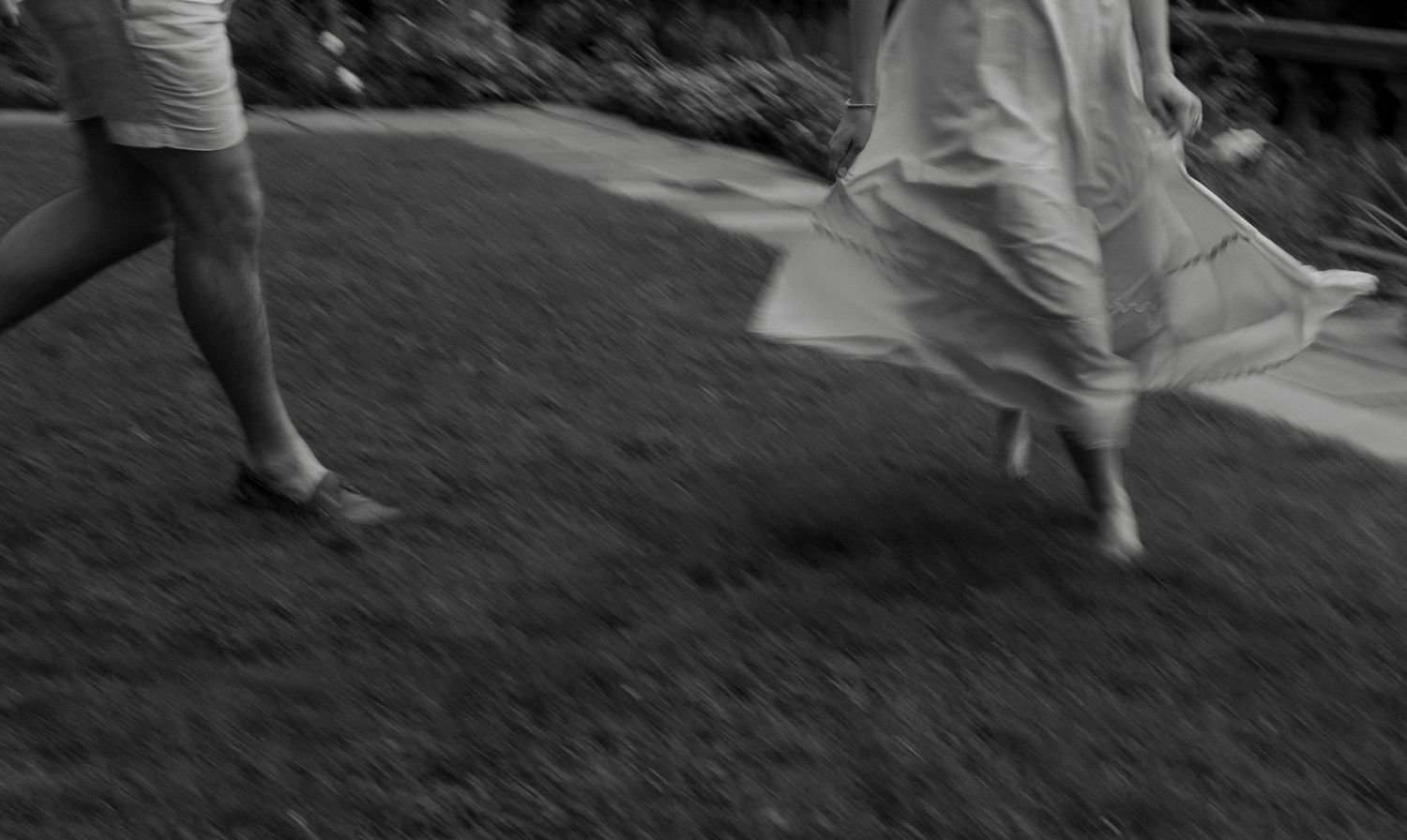 Black and white blurred motion photo of couple running barefoot together across a lawn.