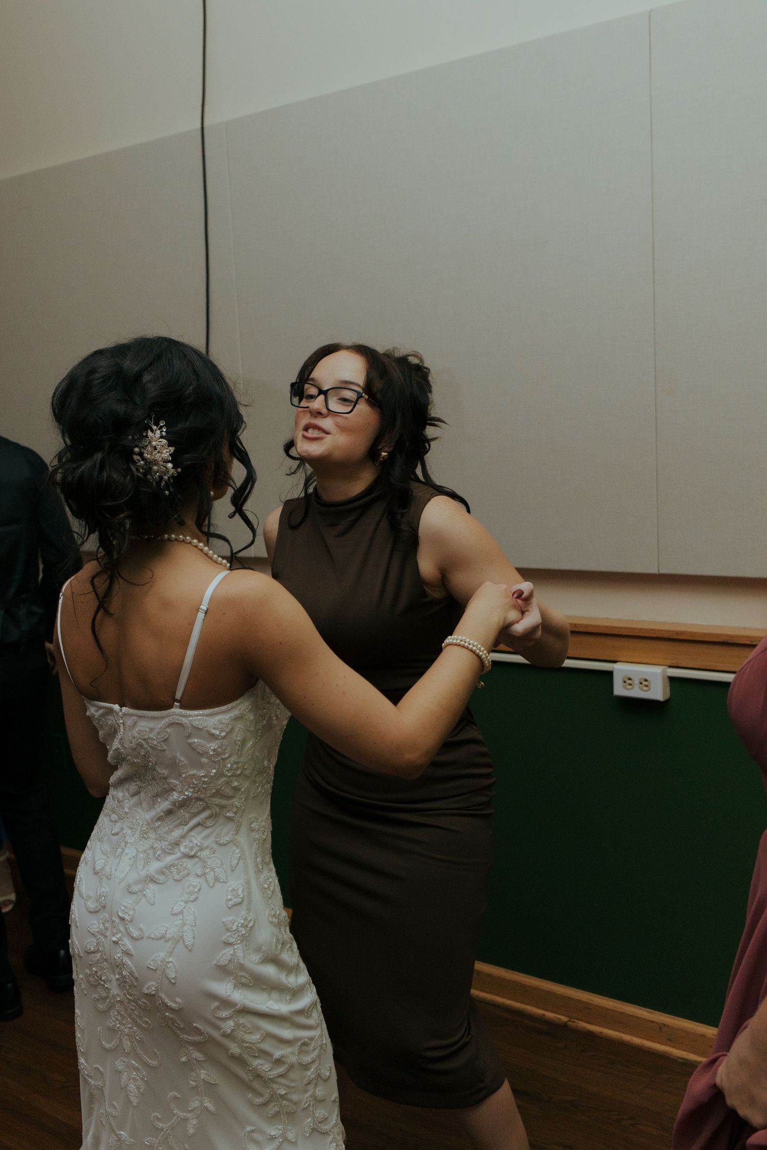 Bride dancing with female guest in olive dress at wedding reception.