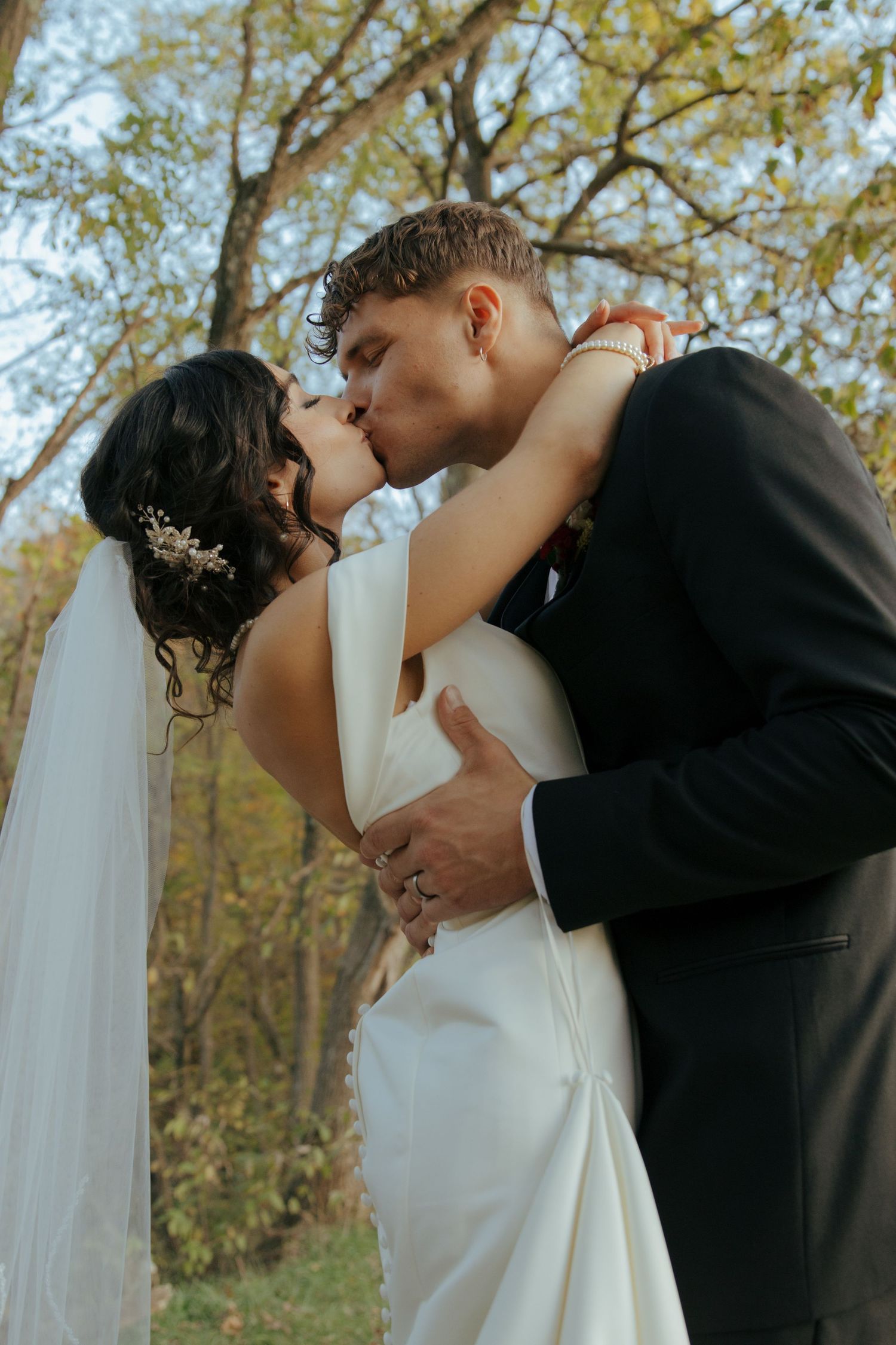 Bride and groom sharing romantic kiss outdoors surrounded by autumn foliage.