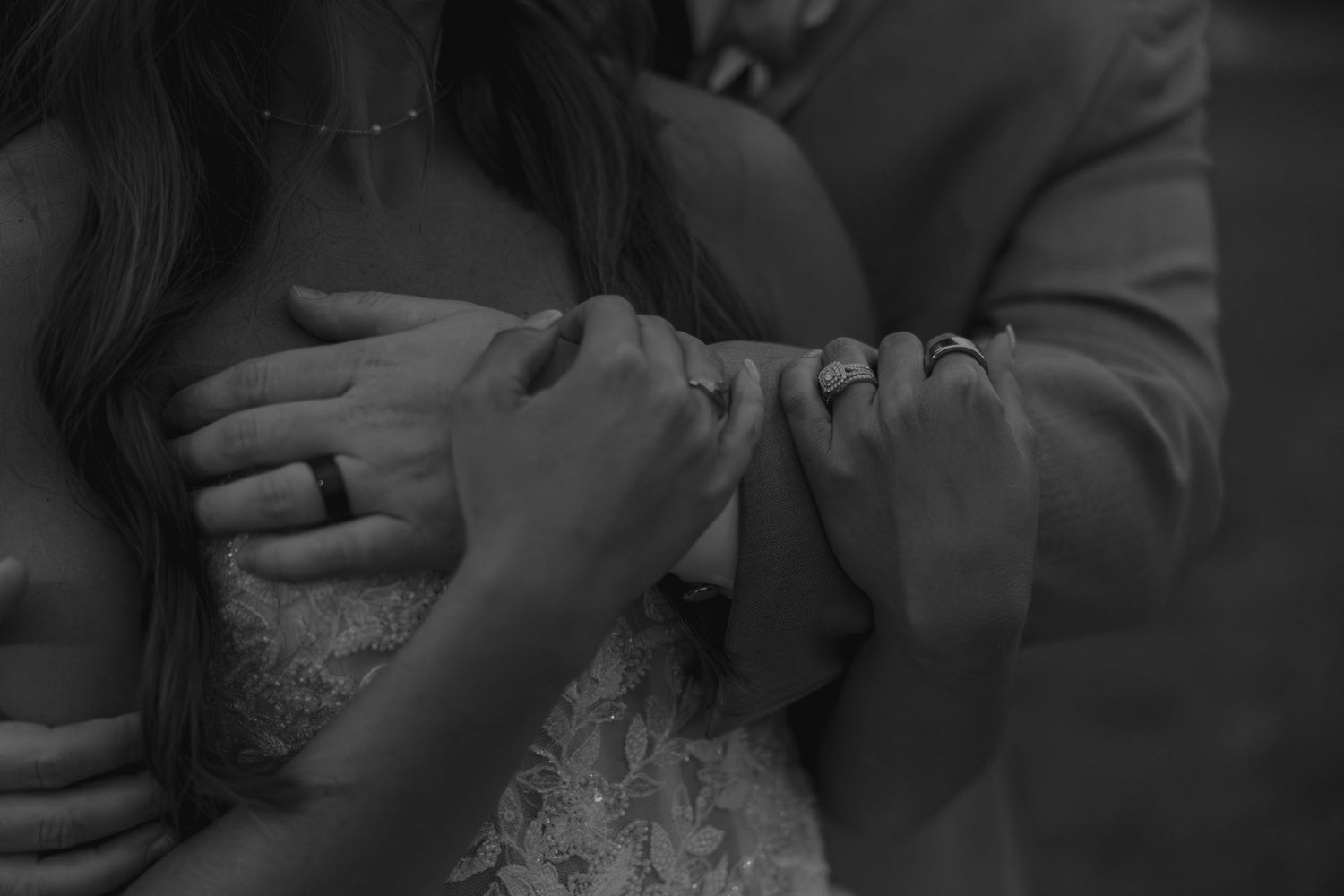Black and white wedding photo of bride and groom holding hands, showing wedding rings in elegant close-up.