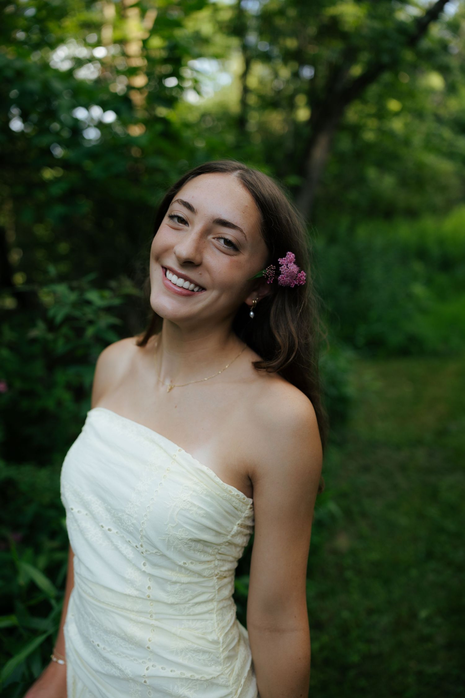 Smiling woman in white strapless dress with pink flower in hair.