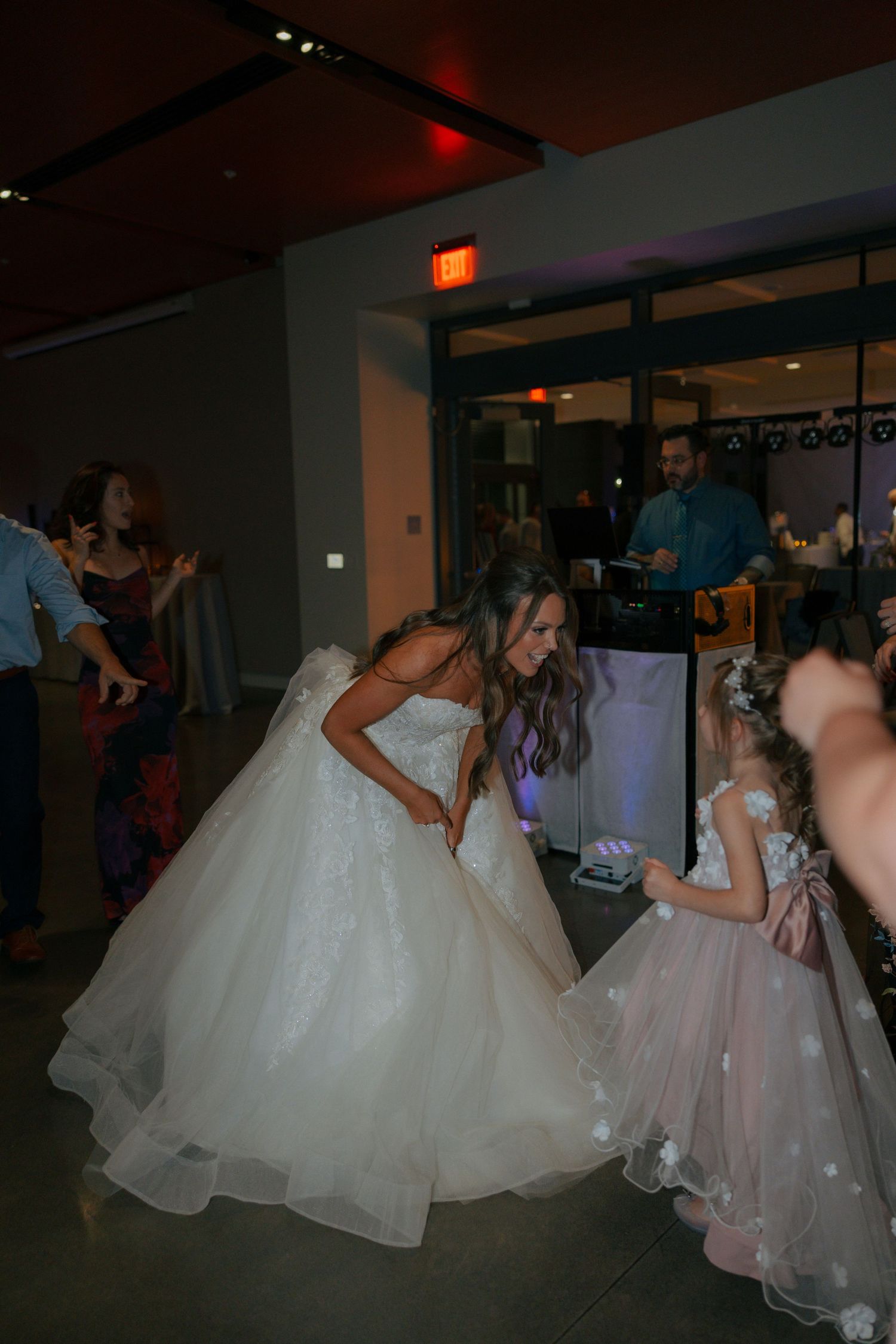 Bride in white ball gown dancing with young flower girl in pink dress at wedding reception celebration.
