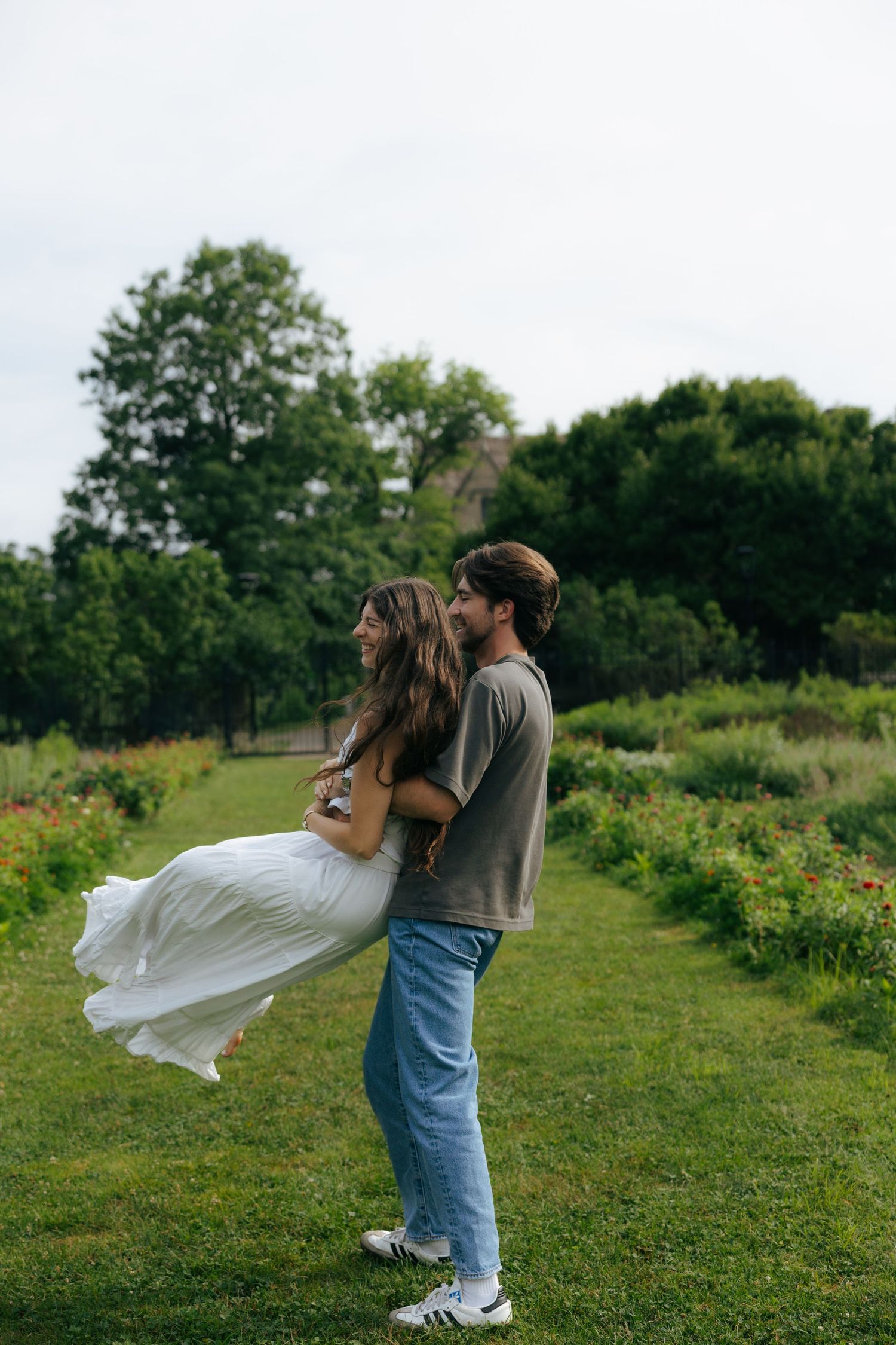 A laughing couple spins together on a green garden path, the woman in a white dress lifted off the ground.