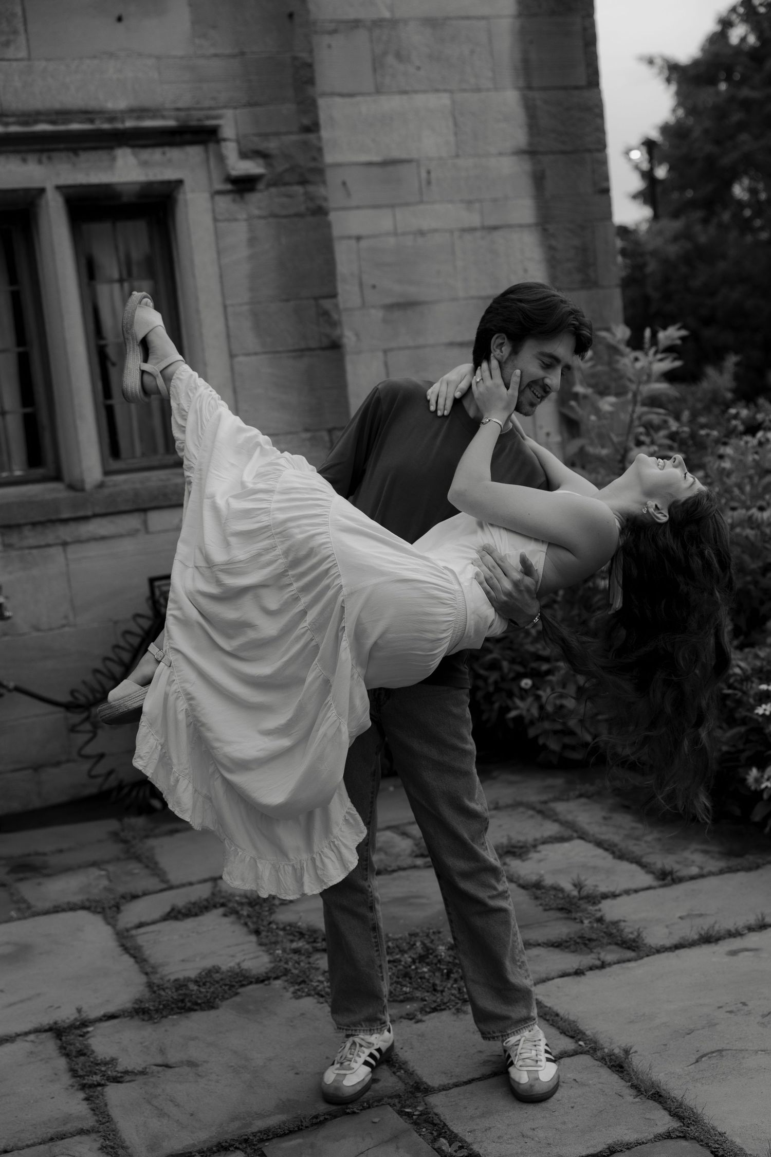 A black and white photo of a man dipping a woman in a white dress dramatically in a stone courtyard.
