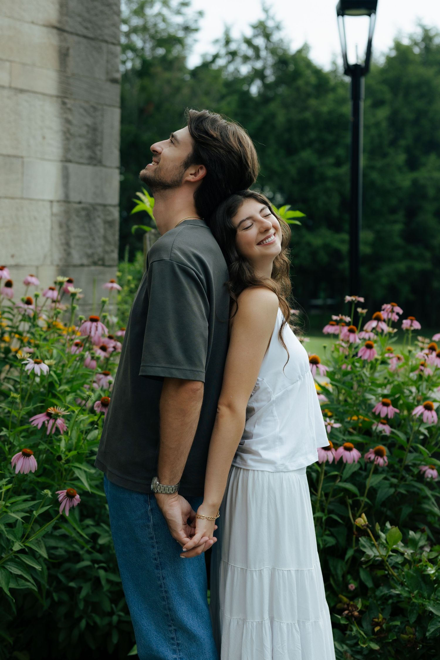 Couple holding hands back-to-back among pink echinacea flowers in a lush garden setting.