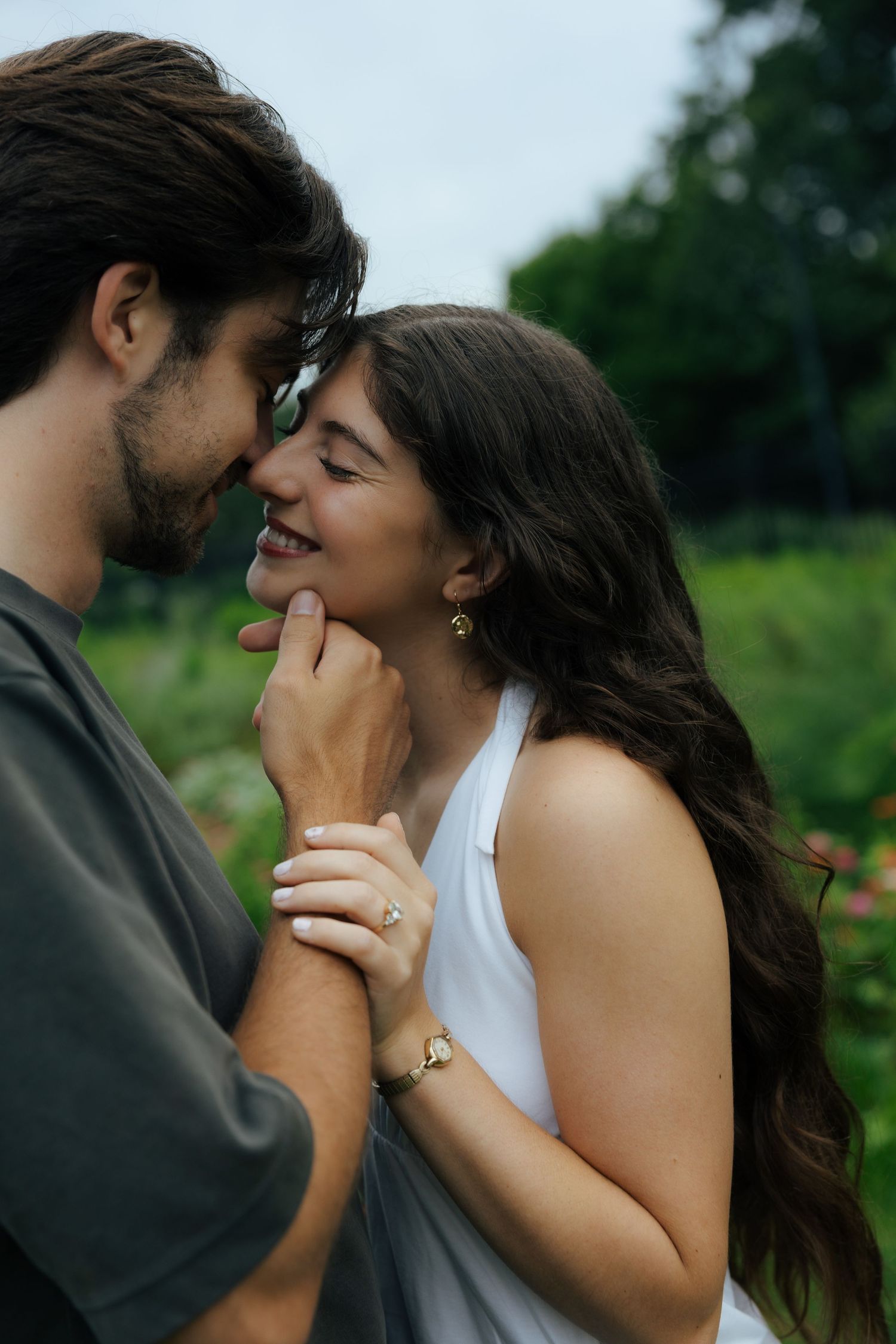 Couple sharing a tender moment, woman smiling as man gently holds her chin in a lush green garden.