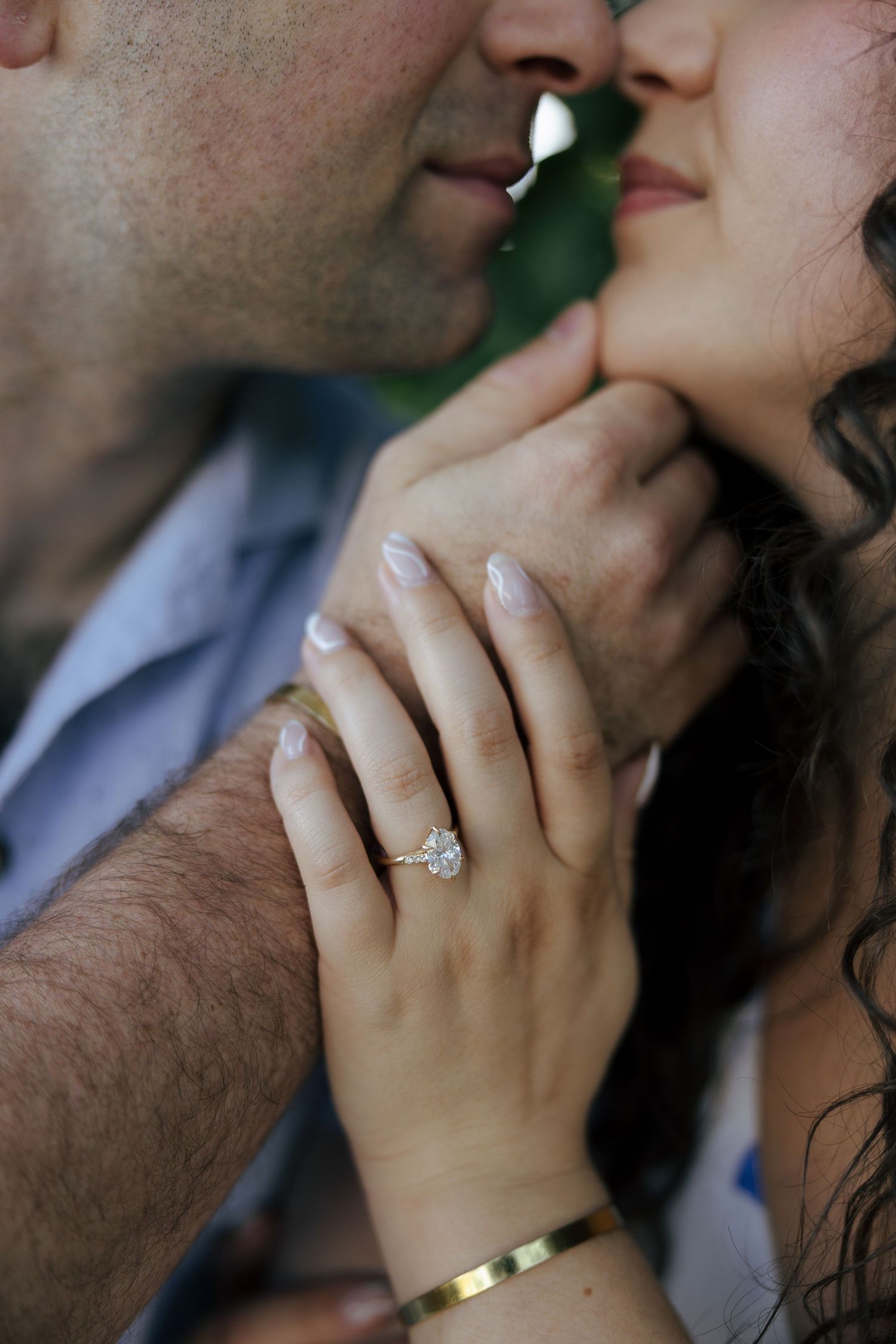 Close-up of elegant diamond engagement ring on womans hand while couple shares a kiss.