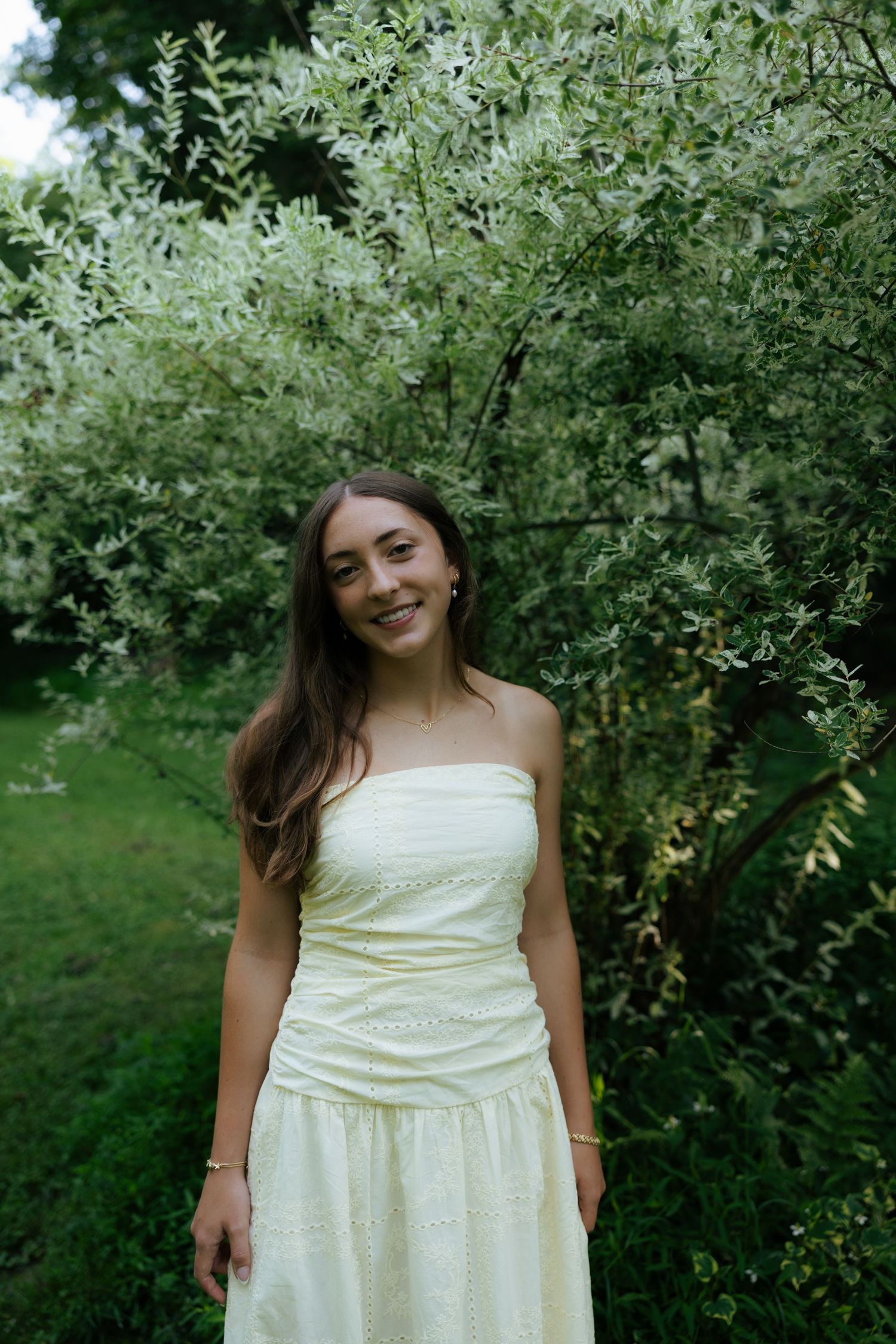 Young woman in cream strapless dress standing by white flowering shrub.