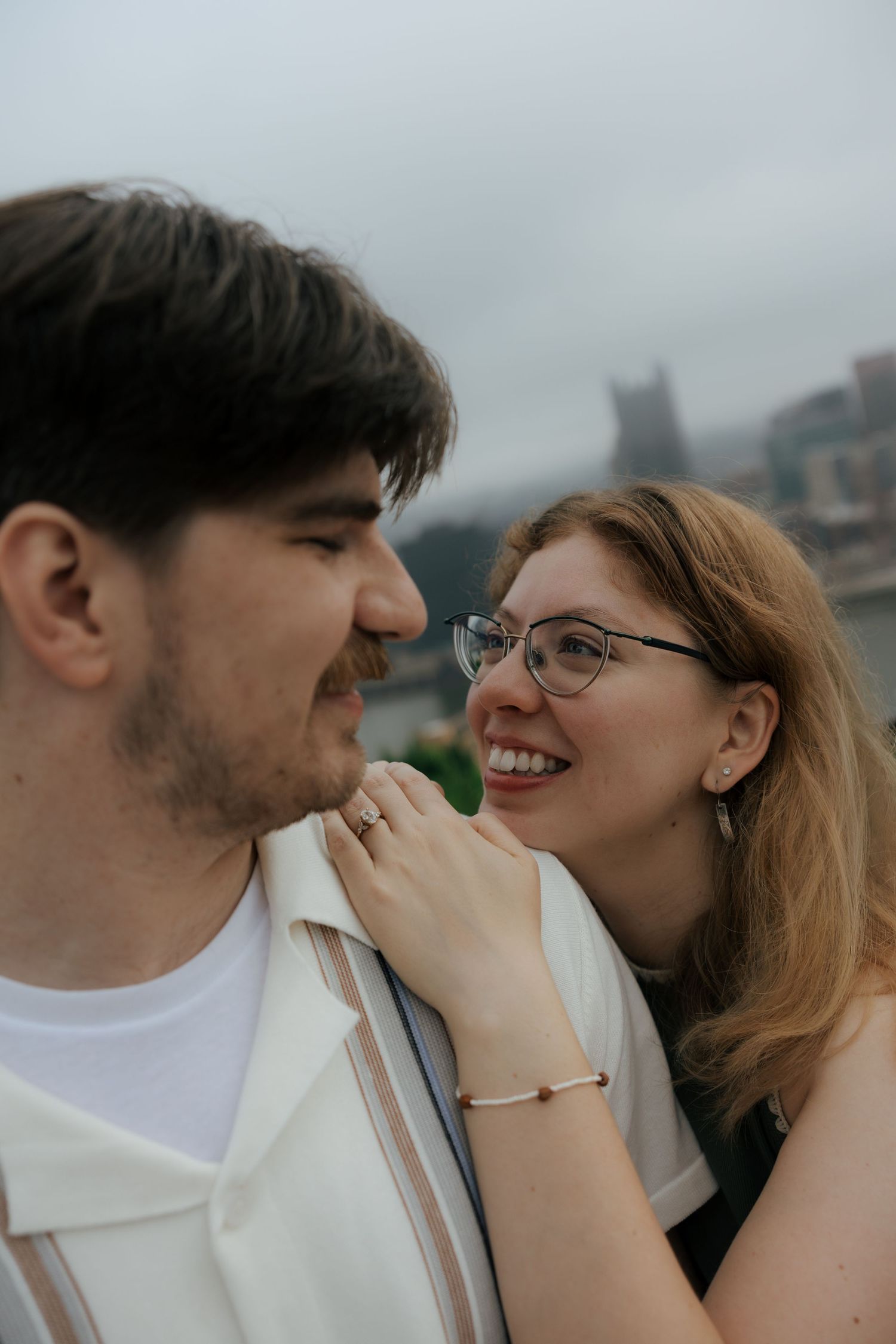 Smiling woman with glasses gazing at her partner during an outdoor engagement photo session.