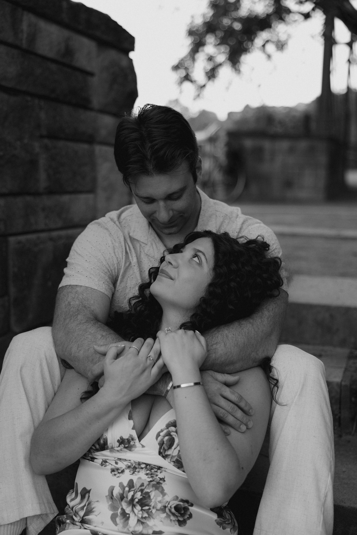 A black and white romantic portrait of a couple sitting on stone steps, the man tenderly embracing the woman.
