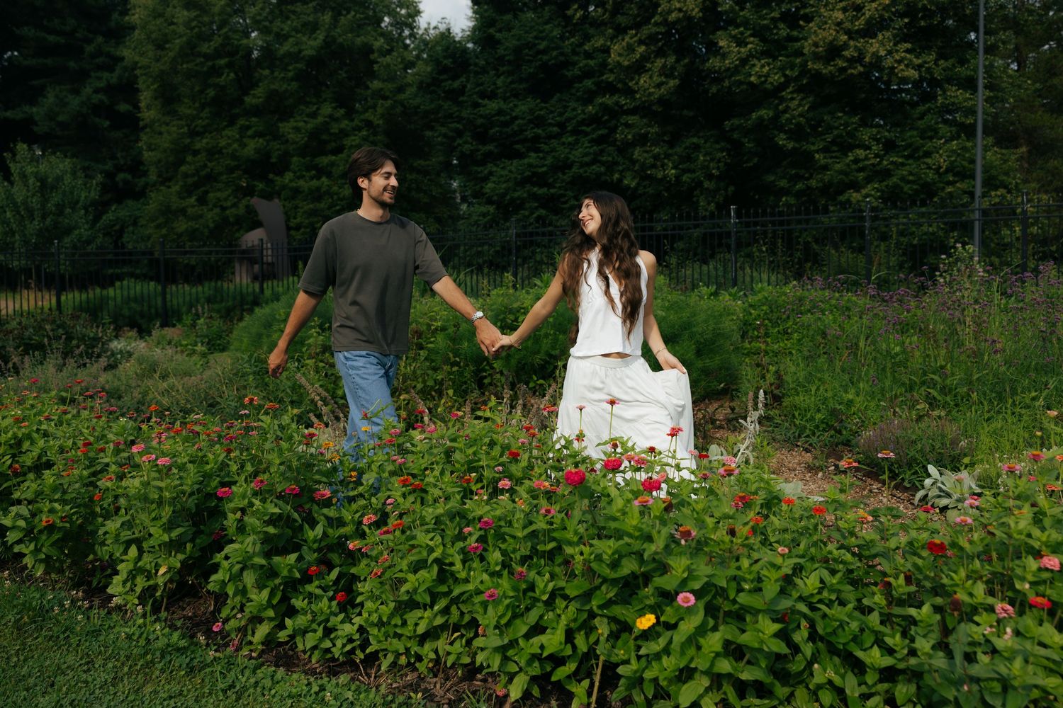 Couple holding hands while walking through a vibrant garden path lined with colorful flowers.