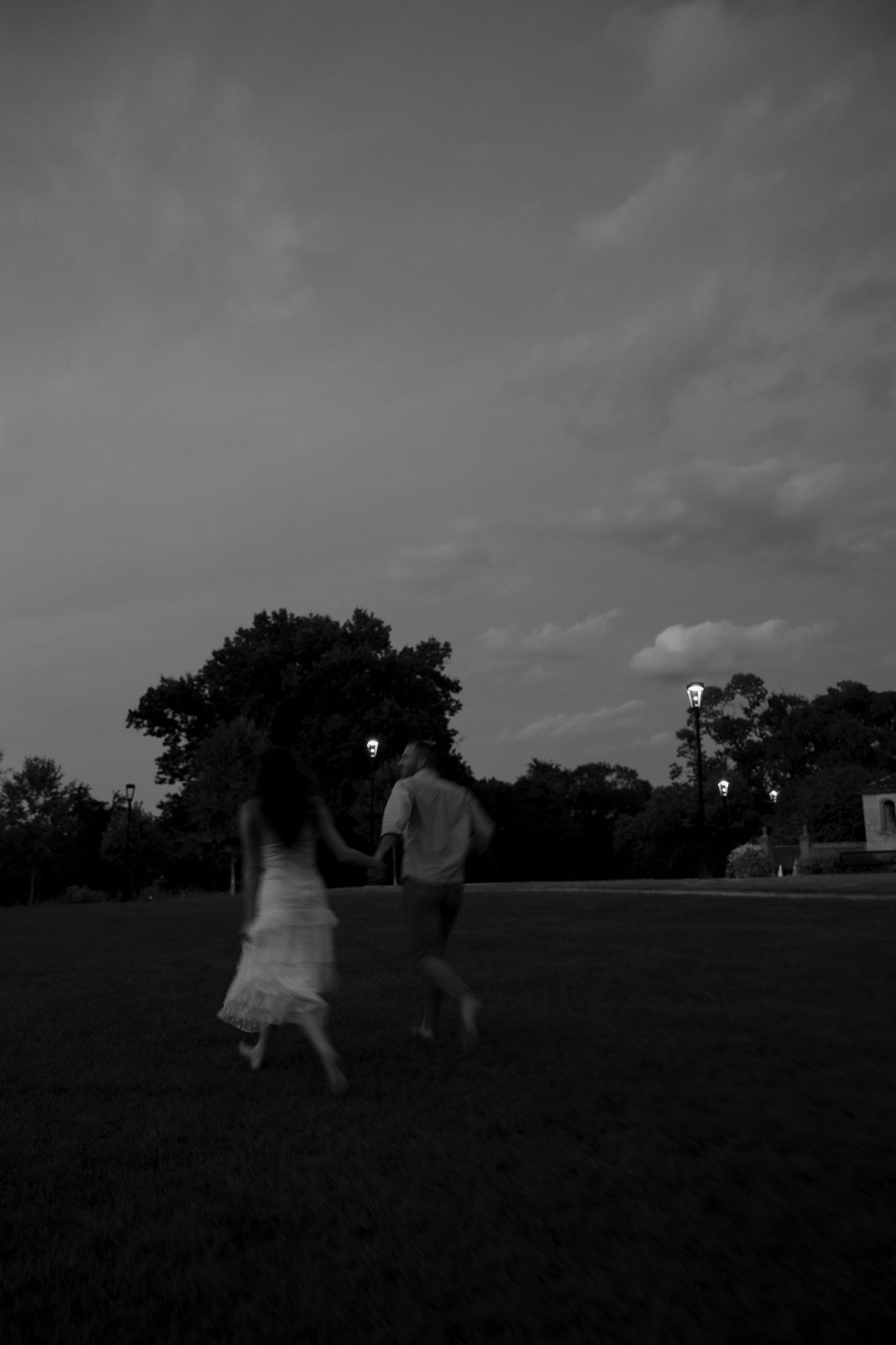 Black and white silhouette of couple running hand in hand across open field at dusk.