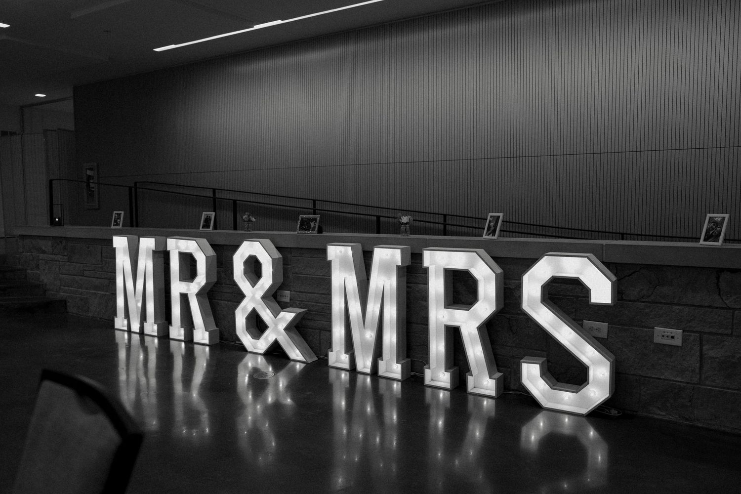 Black and white photo of illuminated MR & MRS marquee letters at a wedding venue reception hall.